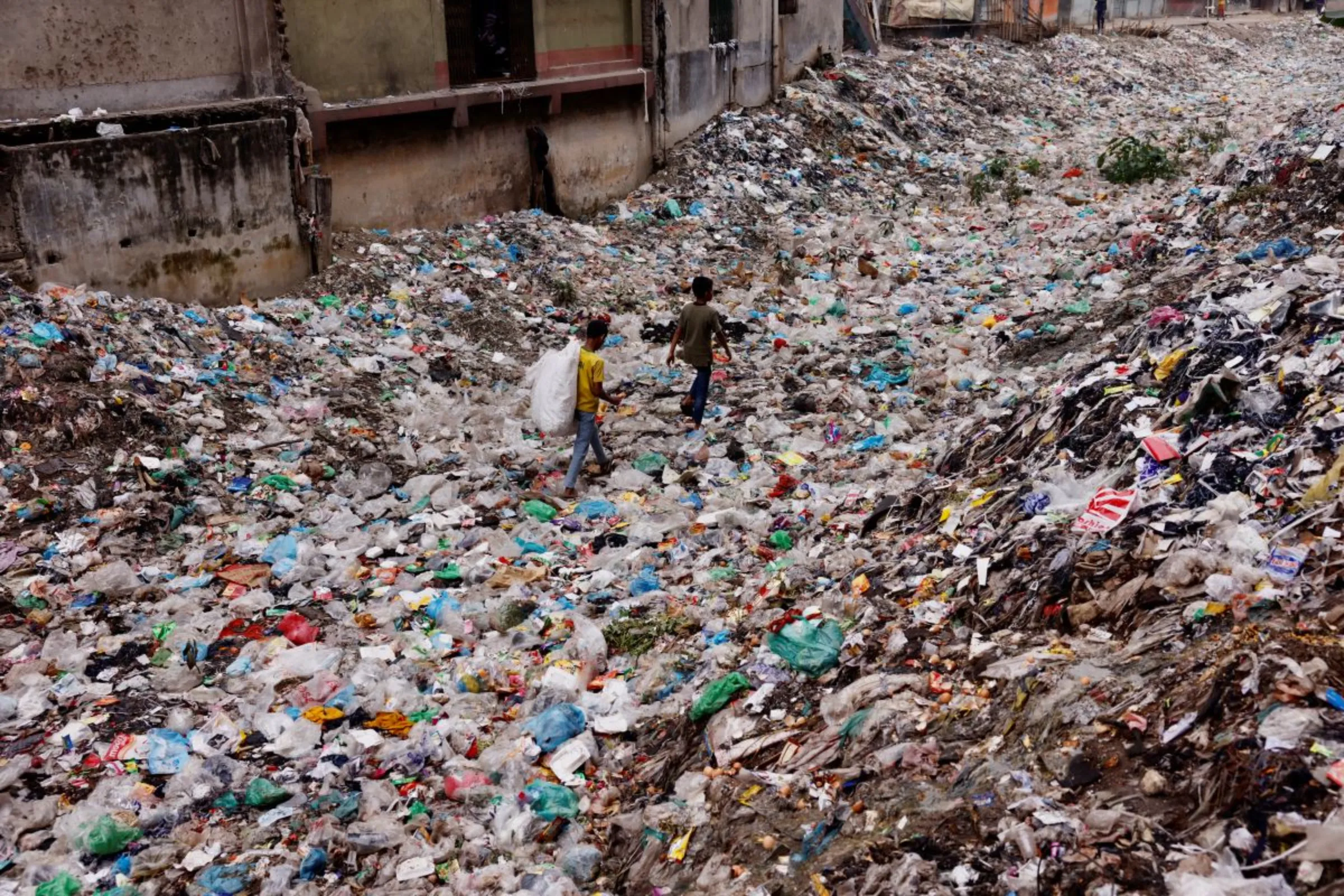 Children walk over a polluted area as they collect plastic materials in Dhaka, Bangladesh, January 24, 2022