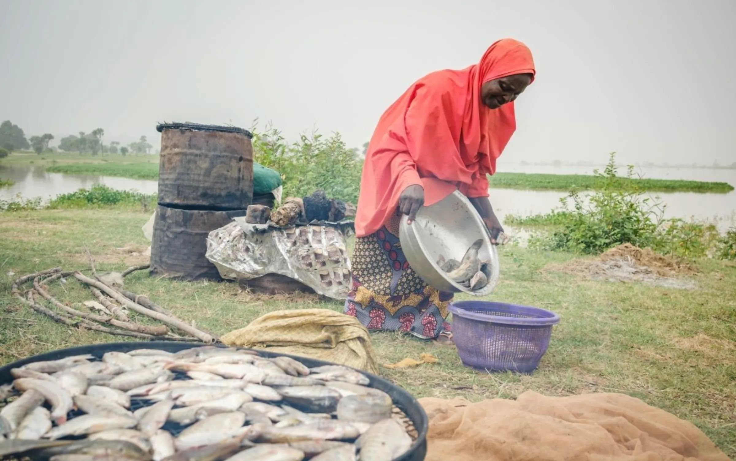 Fish farmer, Faiza Habibu, pours fish into a basket next to Dasin Hausa river in Adamawa, Nigeria. Habibu is a beneficiary of Google climate resiliency project and used the funds to expand her fish farming business. International Rescue Committee (IRC)/Handout via Thomson Reuters Foundation