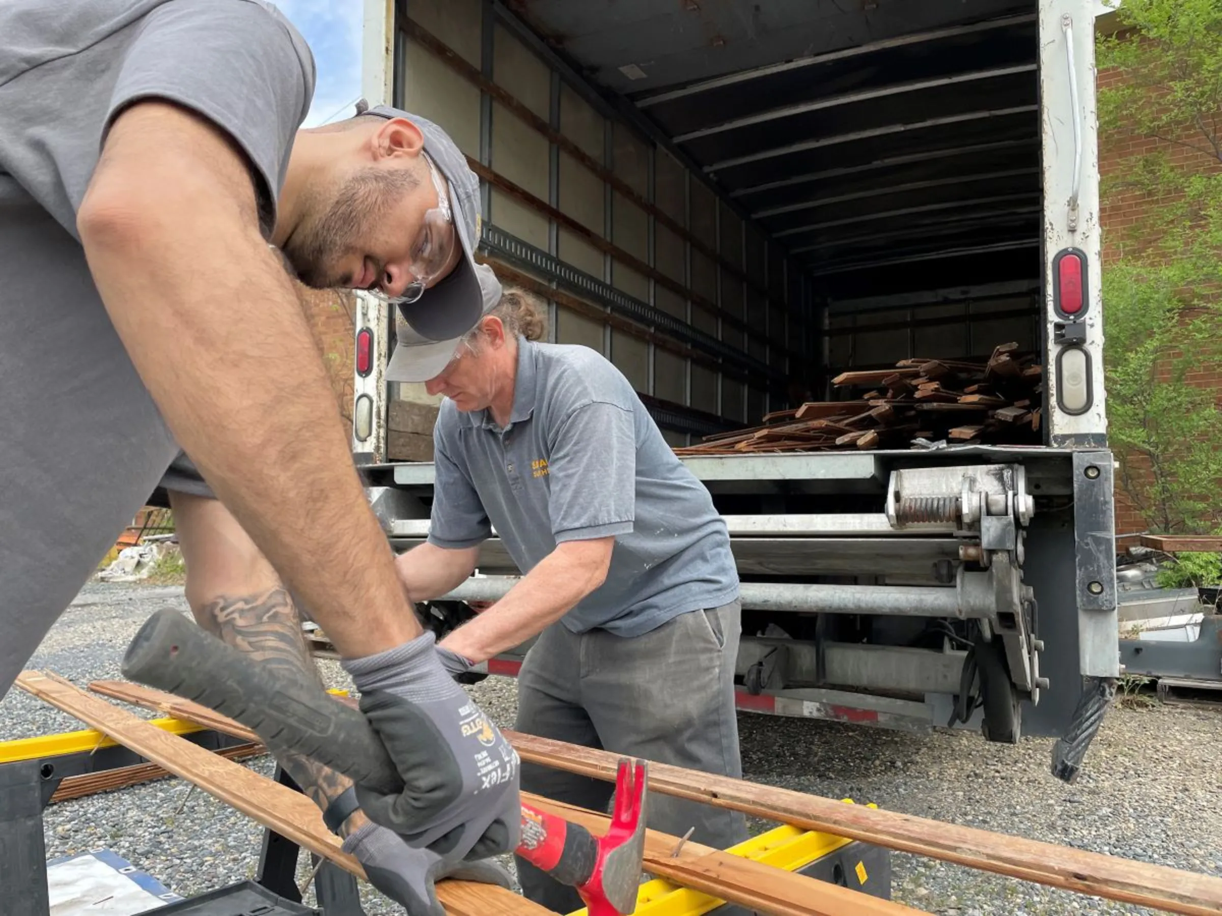 Luis Torres, left, and Tom Patzkowski remove nails from salvaged flooring in Edmonston, Maryland, in April 2023. Community Forklift/Handout via Thomson Reuters Foundation