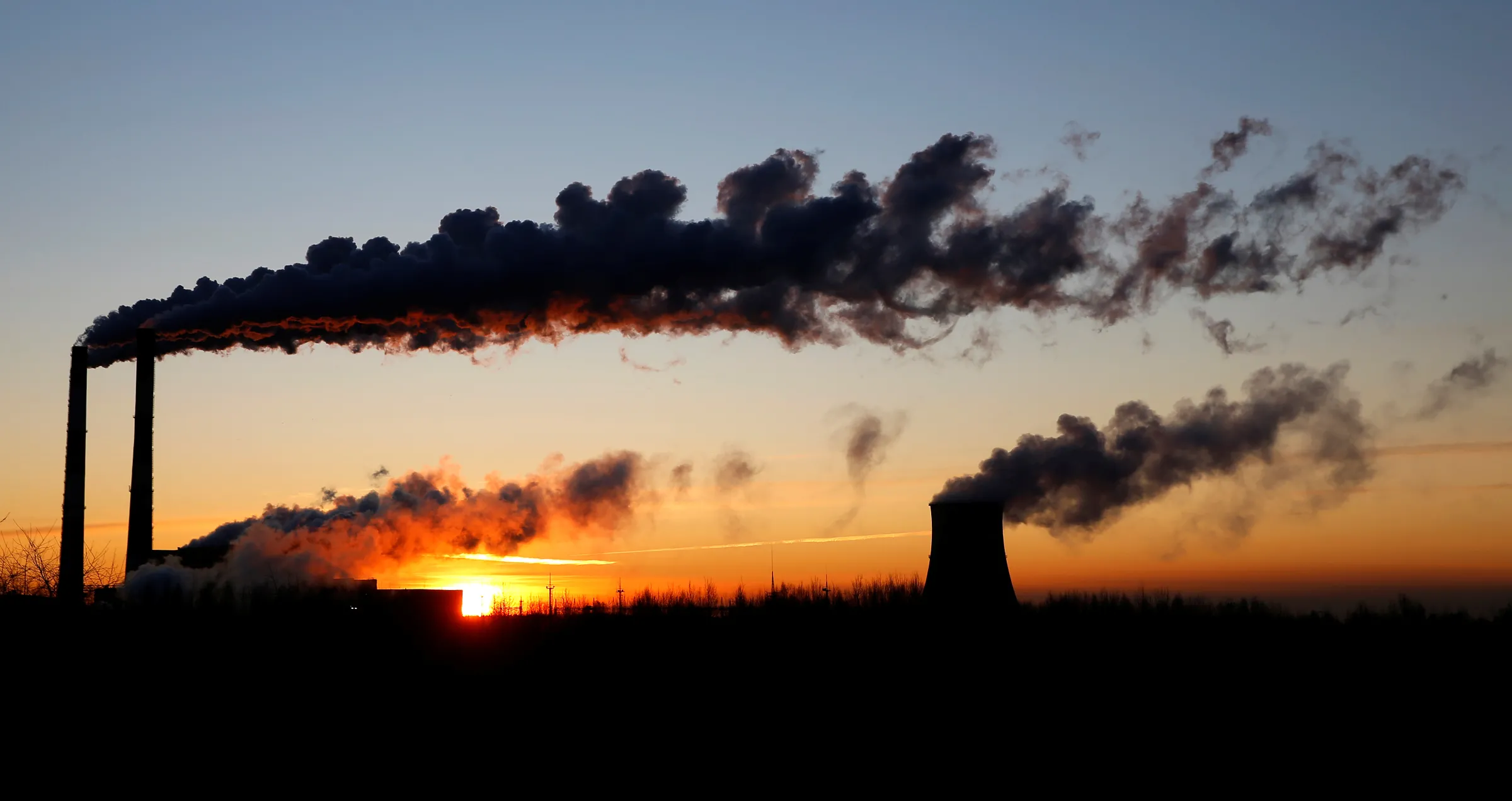 Smoke from factory chimneys is silhouetted against the sky