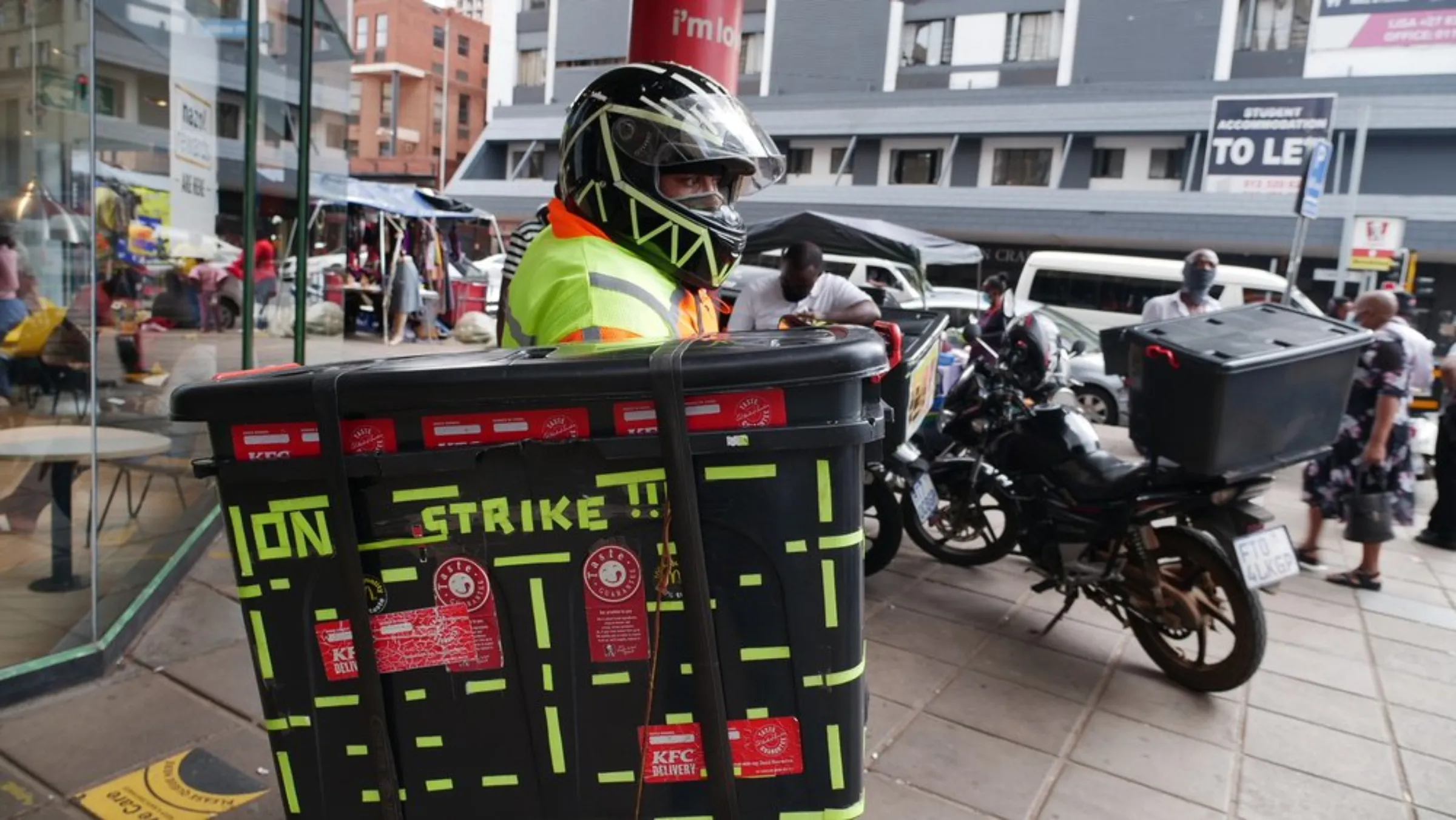 John peers over his food delivery box covered in neon stickers that indicate he was part of the January Uber Eats strike protesting delivery fee cuts across South Africa. Drivers say the fee cuts together with lost income during lockdown mean they have to spend longer hours on the road to make ends meet. February 9, 2020. Thomson Reuters Foundation/Kim Harrisberg