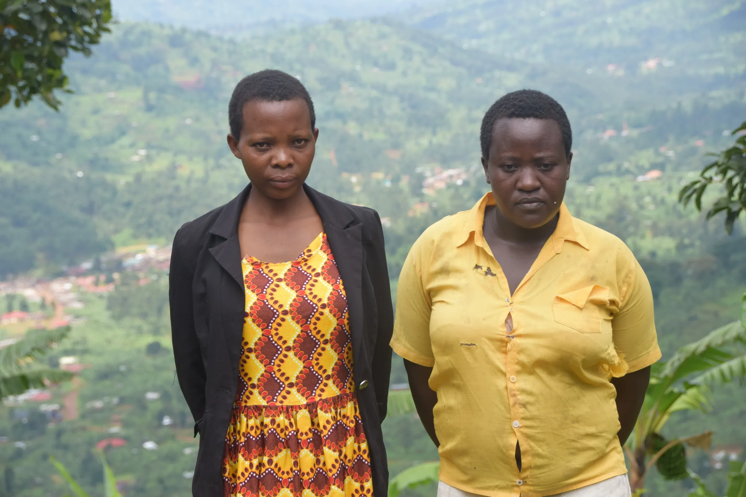 Two women wearing bright colours stand side by side on a mountainside