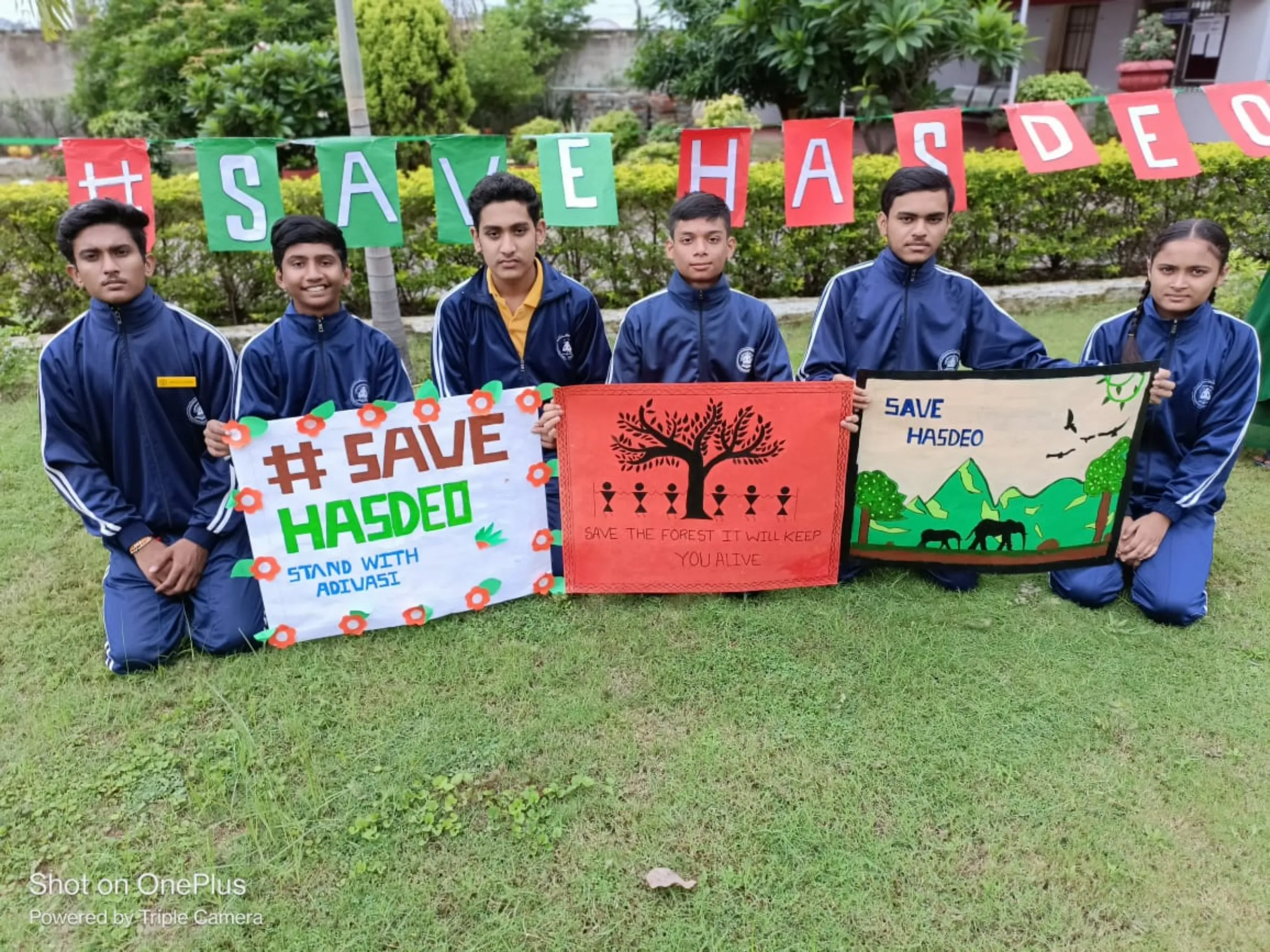 Students in uniform kneel in a line holding banners