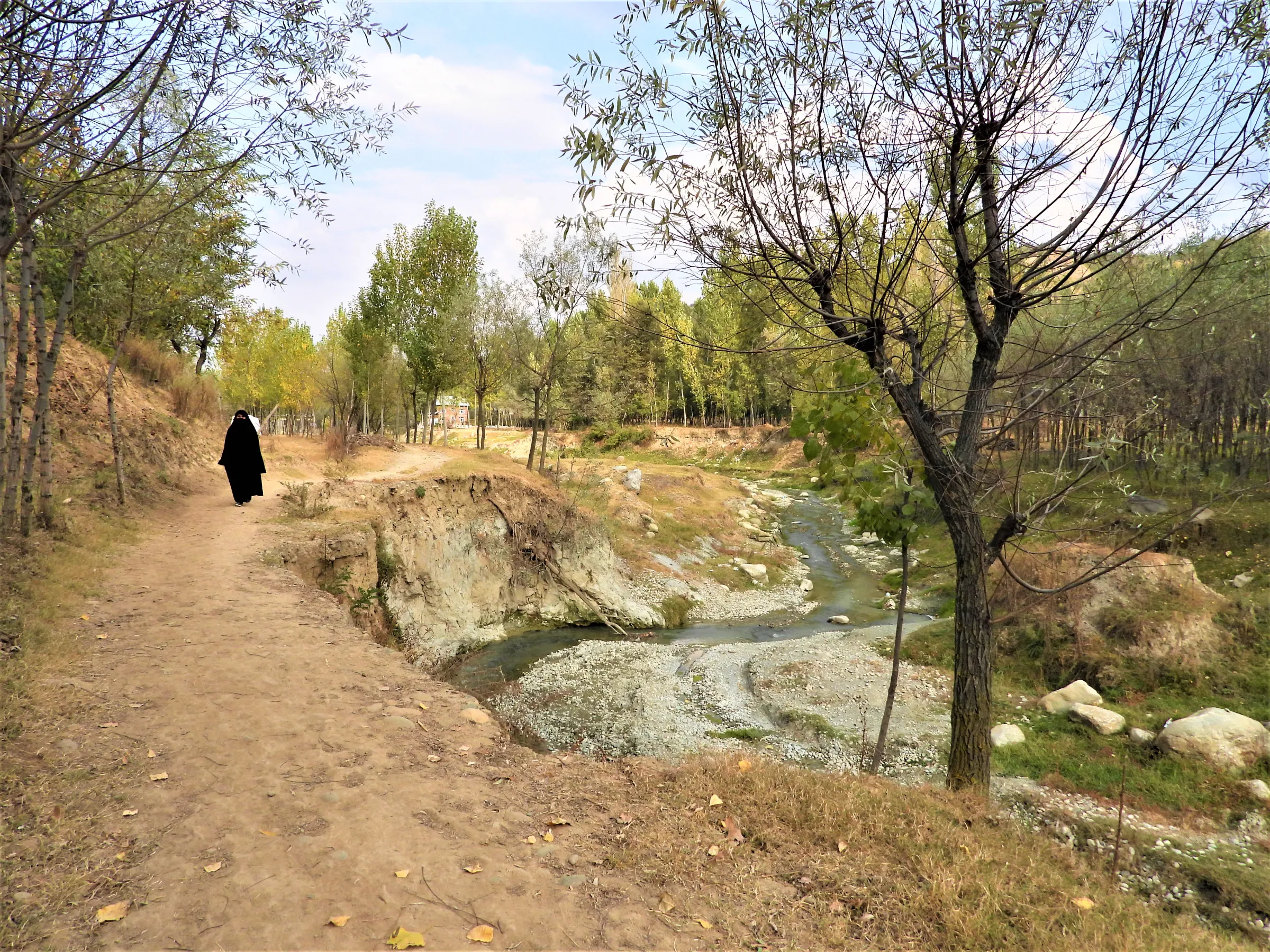 A veiled woman walks on a road damaged by flooding exacerbated by glacial melt, in Kashmir's Chendargund village, India, October 12, 2022