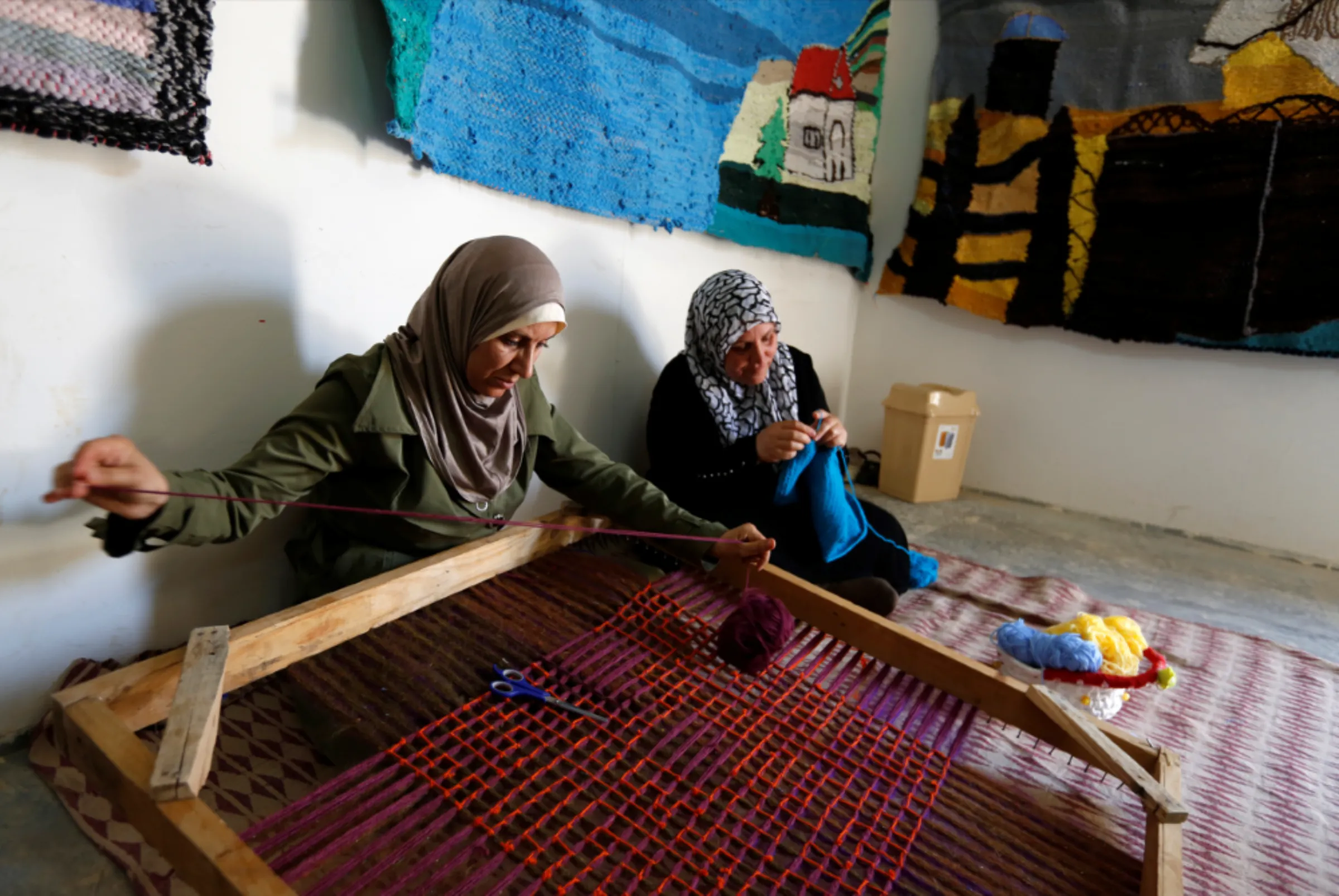 A Syrian woman weaves wool as a colleague knits a baby shawl at a shelter for women built by Italian NGO Building Peace Foundation and run by UN Women at Al Zaatari refugee camp outside the city of Mafraq in Jordan, near the border with Syria, July 17, 2017