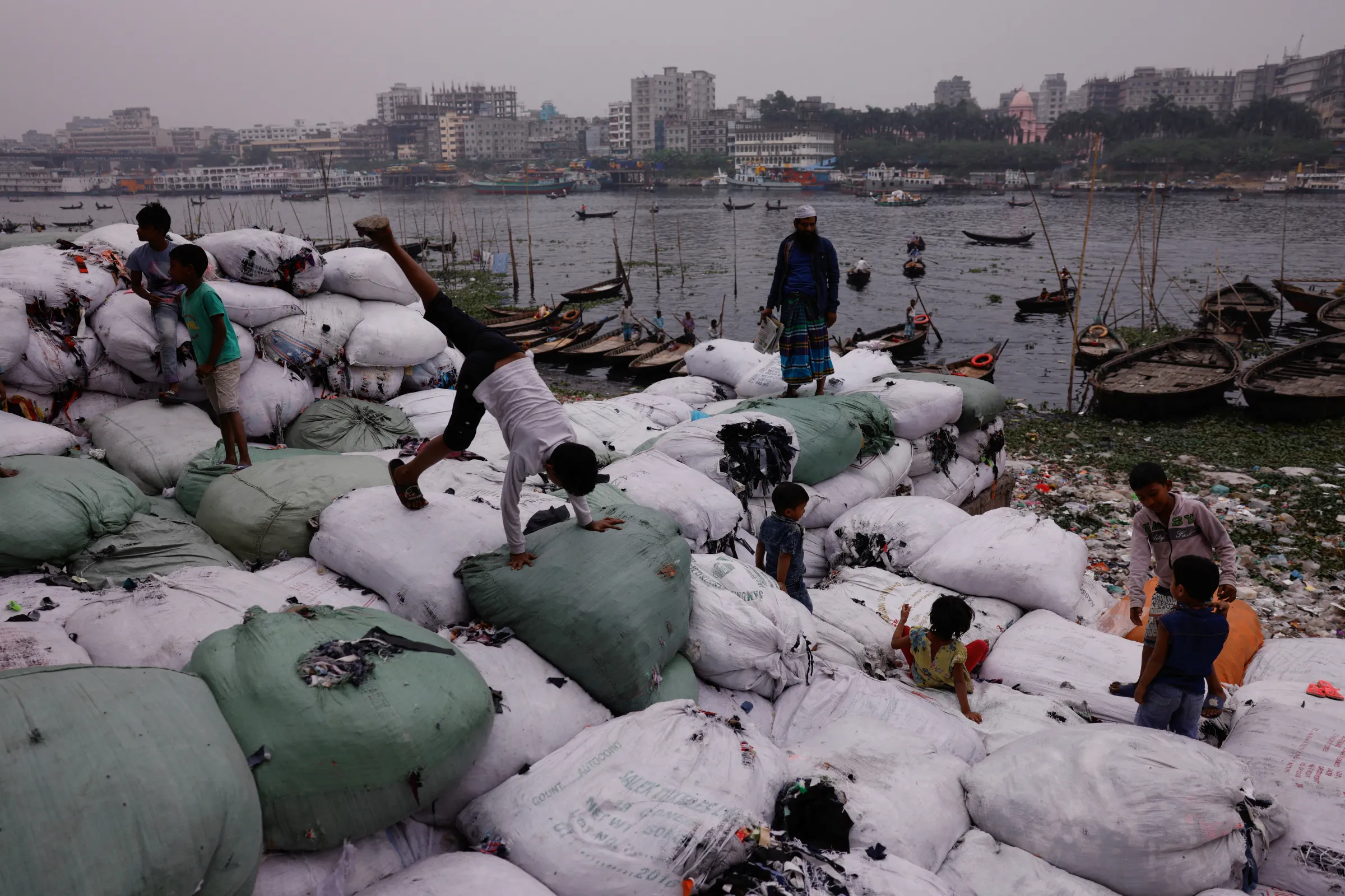 Children play on sacks of garment waste kept by the bank of Buriganga river in Dhaka, Bangladesh, January 24, 2022. REUTERS/Mohammad Ponir Hossain