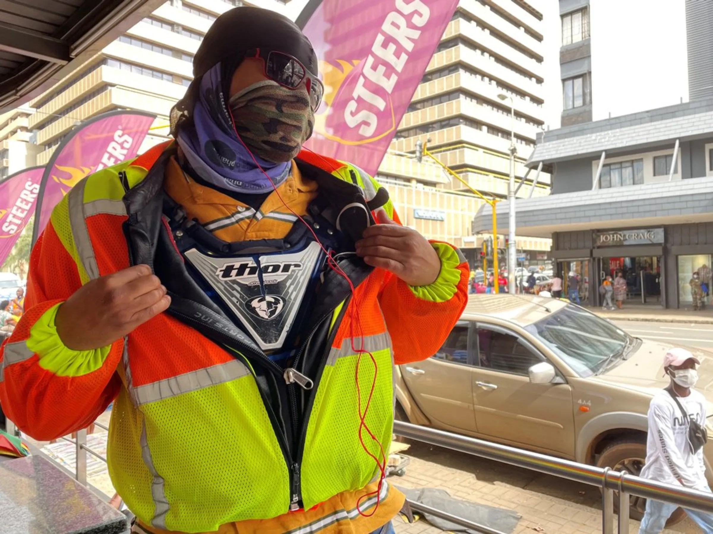 Burundian food courier, John, who fled his country after his family was killed during political conflict, opens up his reflective safety jacket to reveal his protective chest plate that he refuses to drive without. He has been in 15 accidents over 12 years as a driver in Pretoria, South Africa. February 9, 2020. Thomson Reuters Foundation/Kim Harrisberg