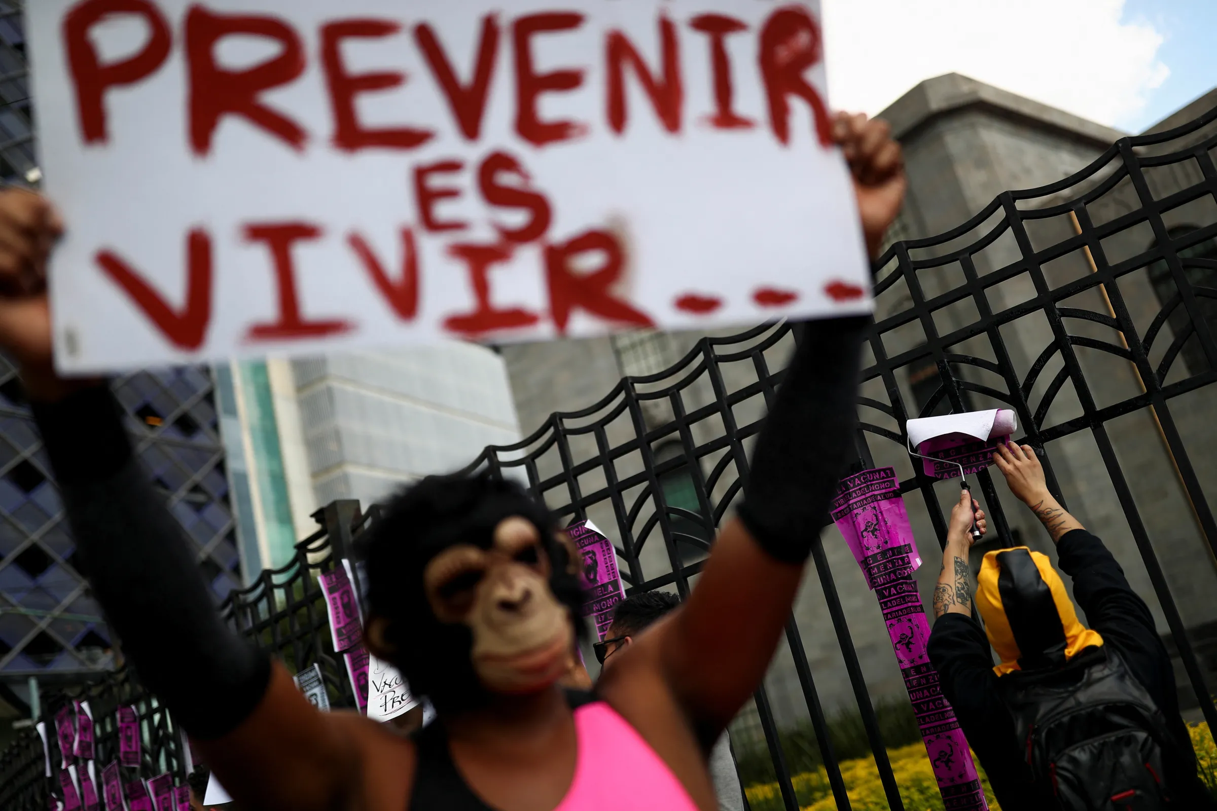 An activist sticks posters on a fence during a protest to call for a stronger response by the government to the monkeypox crisis