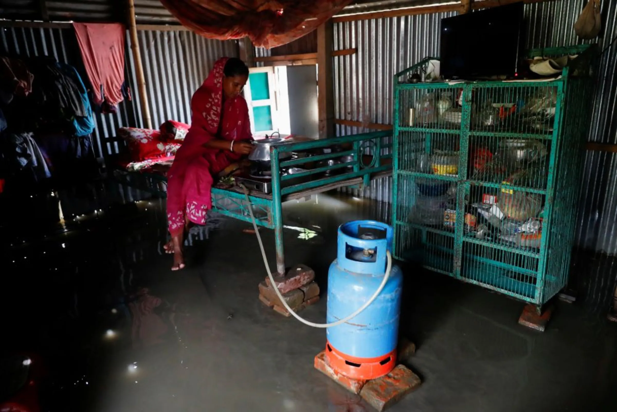 A flood-affected woman uses liquid petroleum gas to cook a meal inside her flooded house in Jamalpur, Bangladesh, July 18, 2020