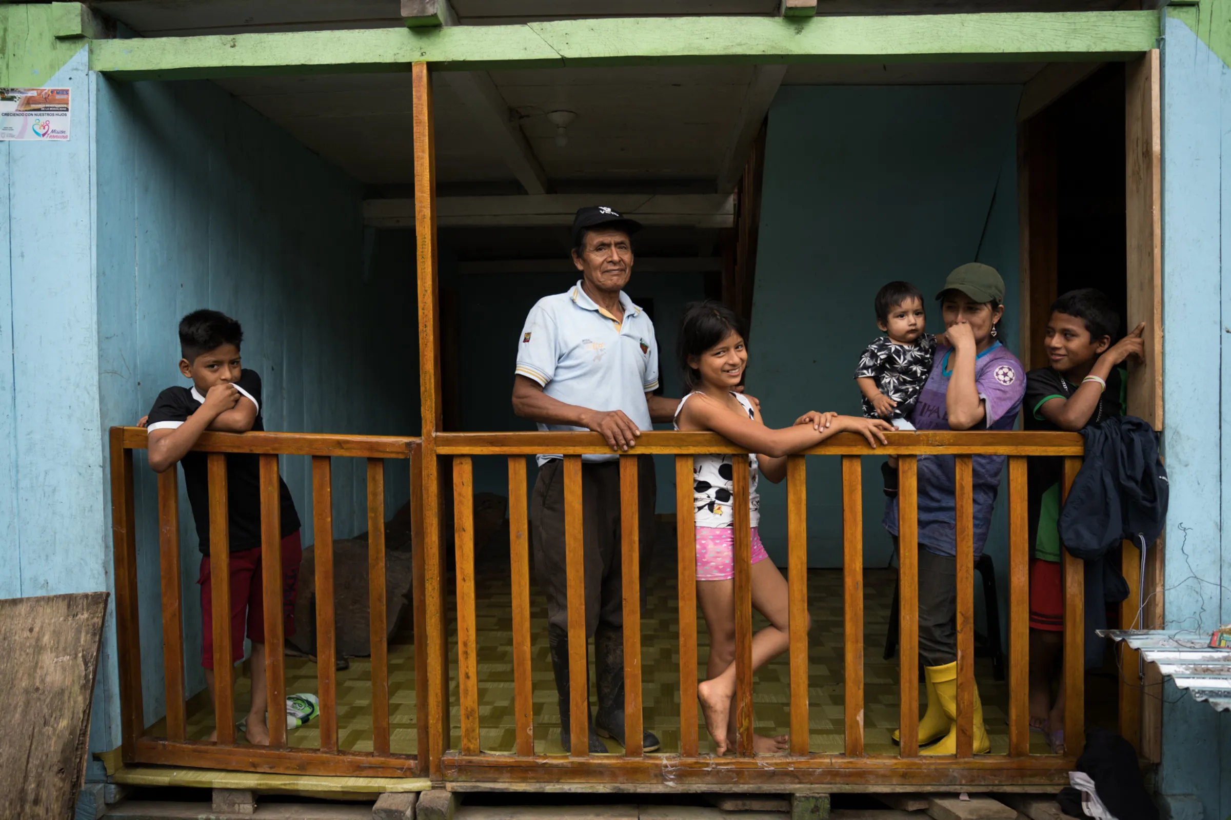 Shuar farmer Carlos Cajamarca stands on his balcony with his daughter, carrying her son, and her three other children