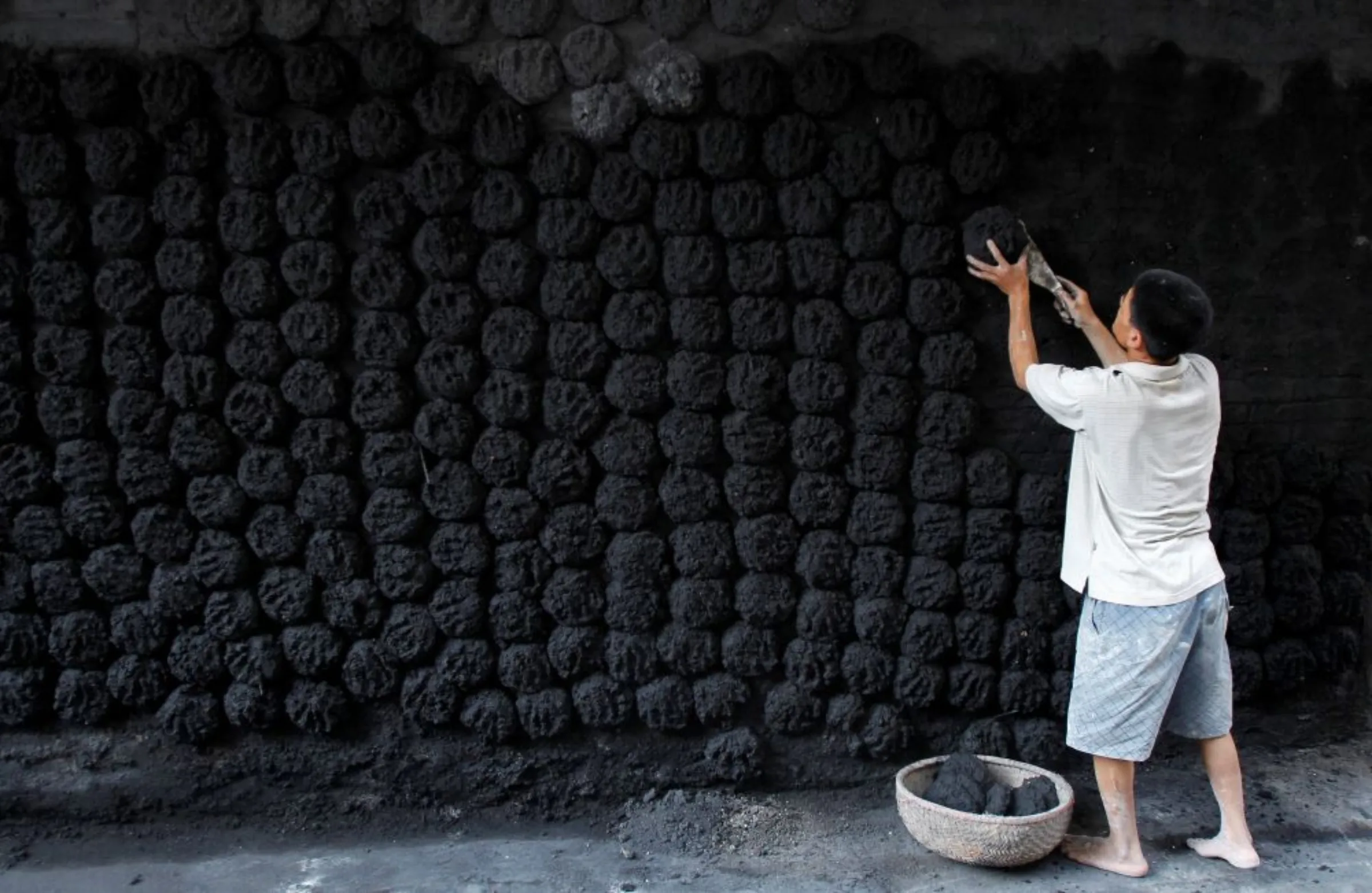 A man lays coal pats, bricks made from coal and paddy, on a wall in Bat Trang village, outside Hanoi November 14, 2011. Bat Trang is renowned for its traditional pottery and ceramics industry and is one of the biggest porcelain makers in Northern Vietnam. Officials are concerned that coal firing in Vat Trang is a cause of pollution which is reaching unacceptable levels.