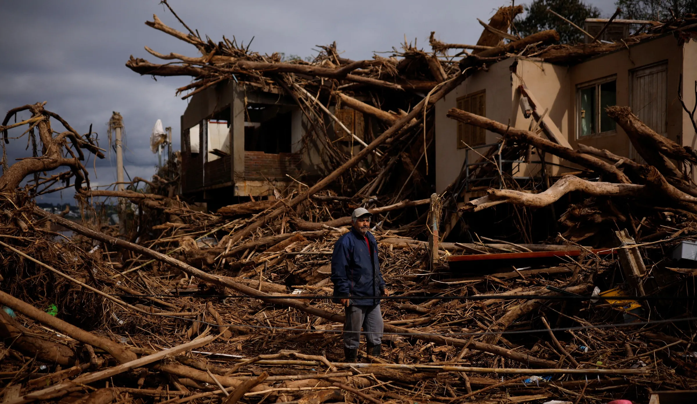 Man stands on tree trunks and branches carried by the water in front of his house damaged by the flood of the Taquari River, in Arroio do Meio, Rio Grande do Sul state, Brazil, May 20, 2024. REUTERS/Amanda Perobelli