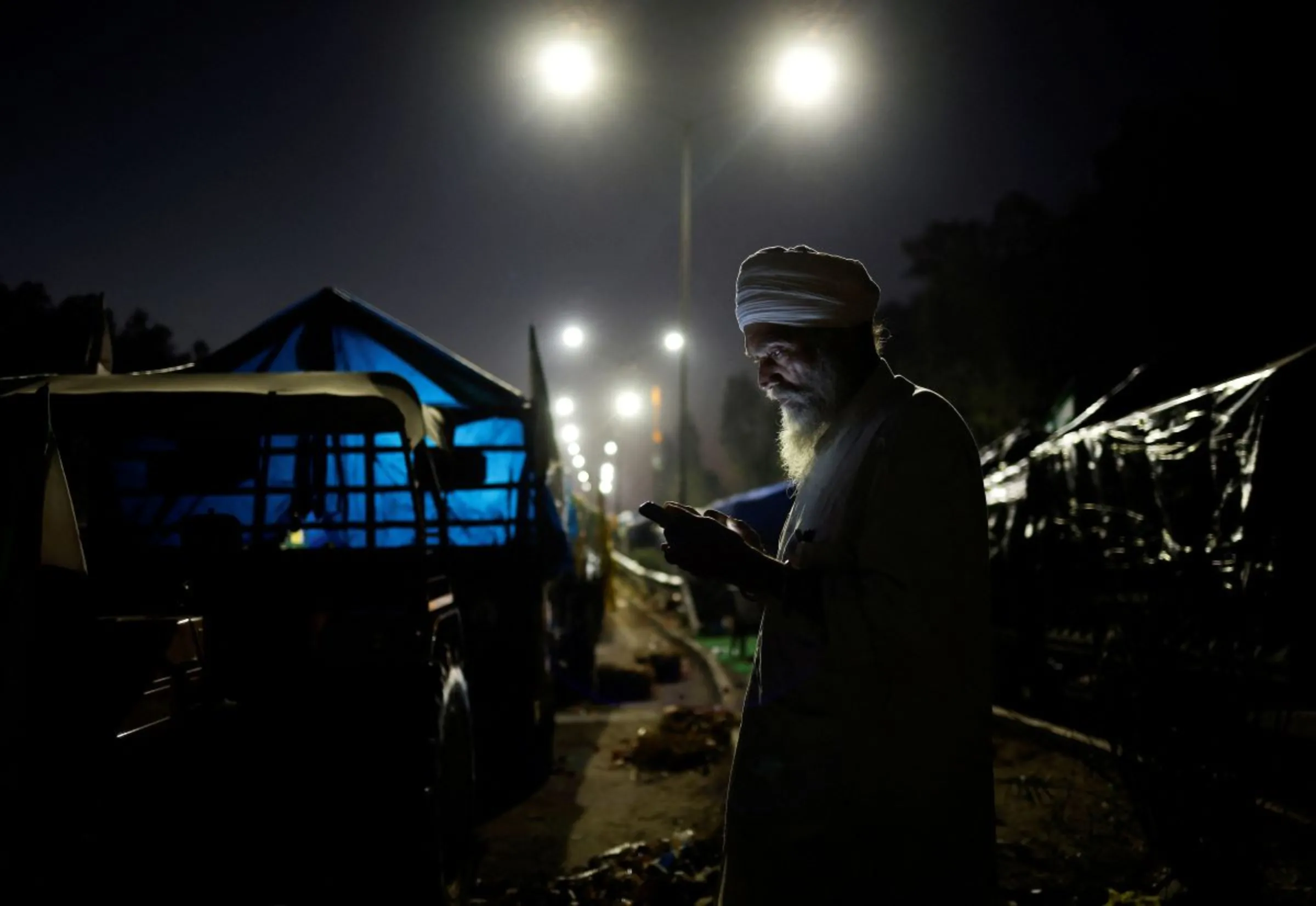 A farmer looks at his phone as he stands next to his tractor trolley as farmers march towards New Delhi to push for better crop prices promised to them in 2021, at Shambhu Barrier, the border between Punjab and Haryana states, India February 22, 2024. REUTERS/Adnan Abidi