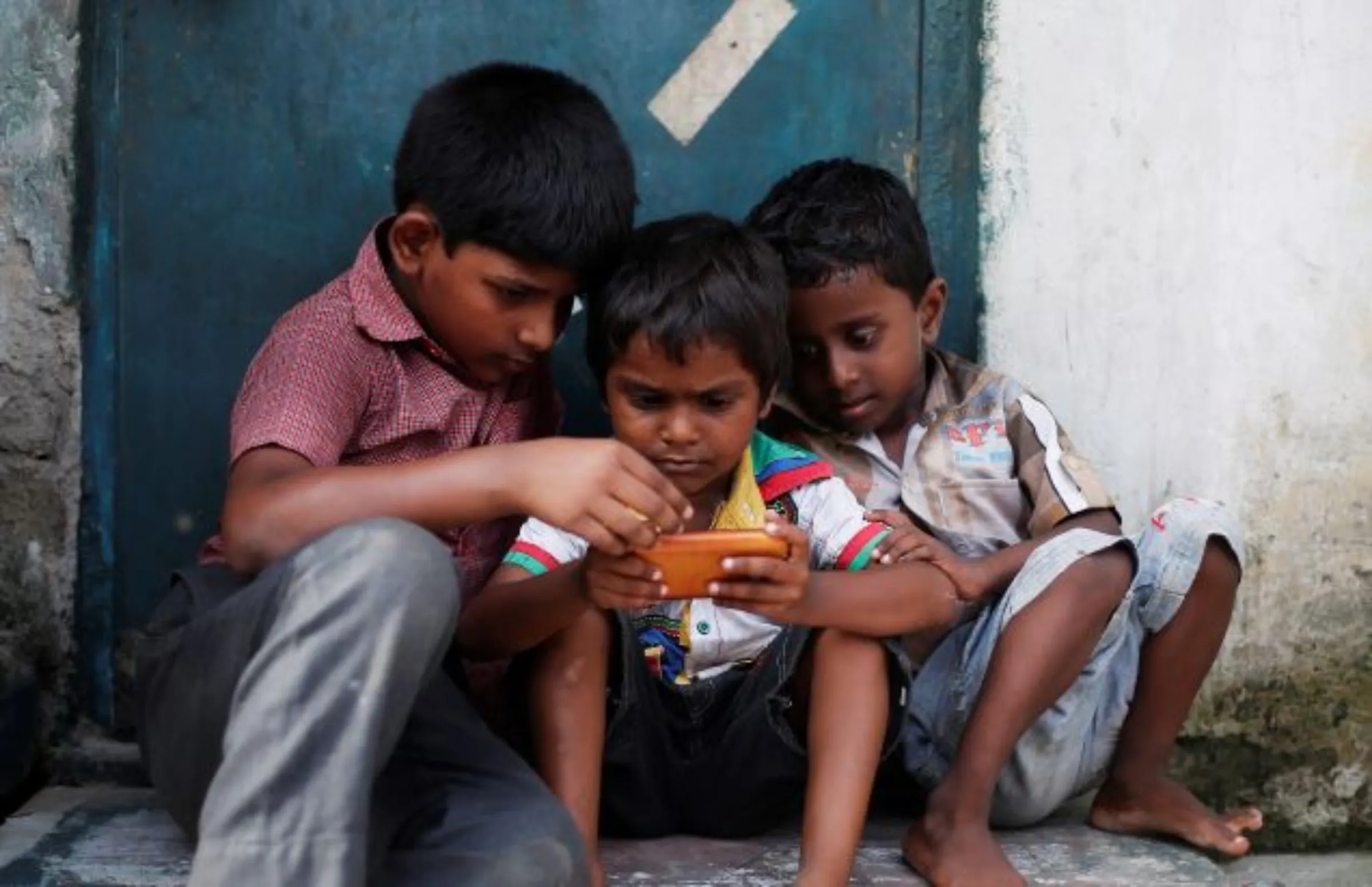 Children play a game on a mobile phone at slum area in New Delhi, India July 4, 2017. REUTERS/Adnan Abidi