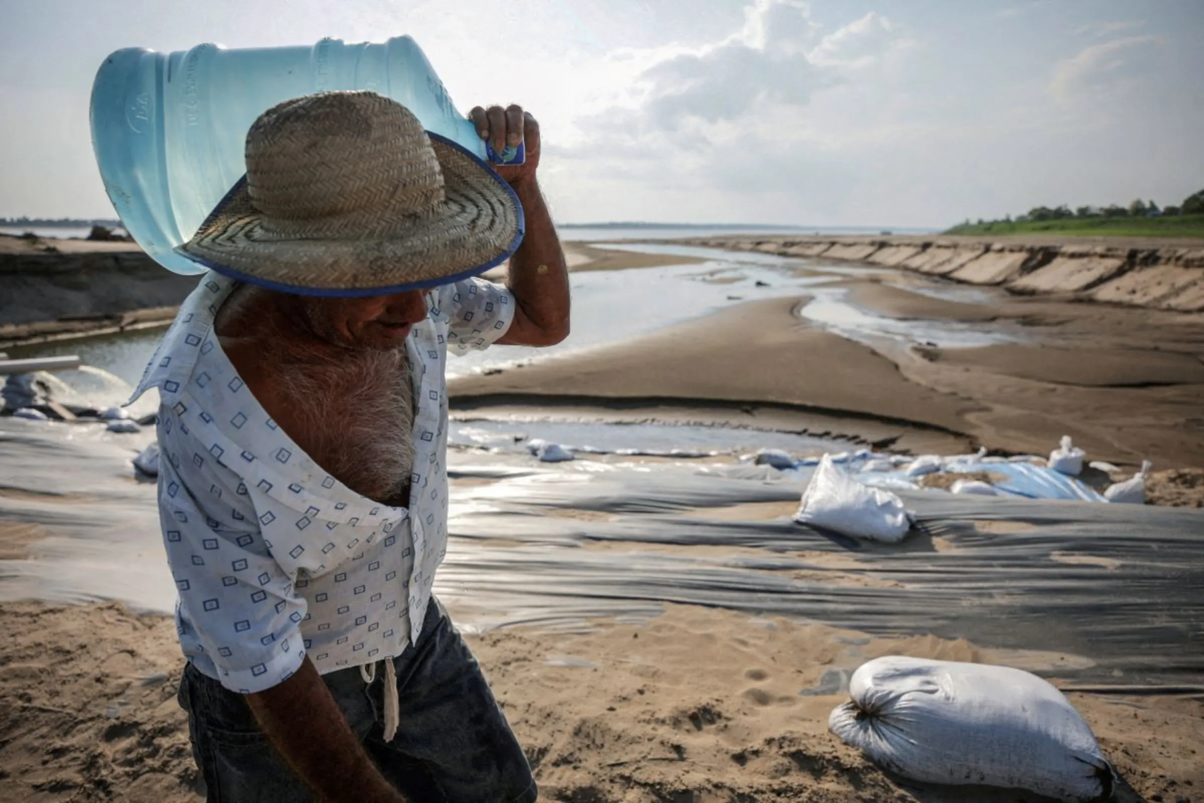A man carries a water jug during a historic drought in the Amazon at the dry riverbed of the Paraua river in Careiro da Varzea, Amazonas state, Brazil October 26, 2023
