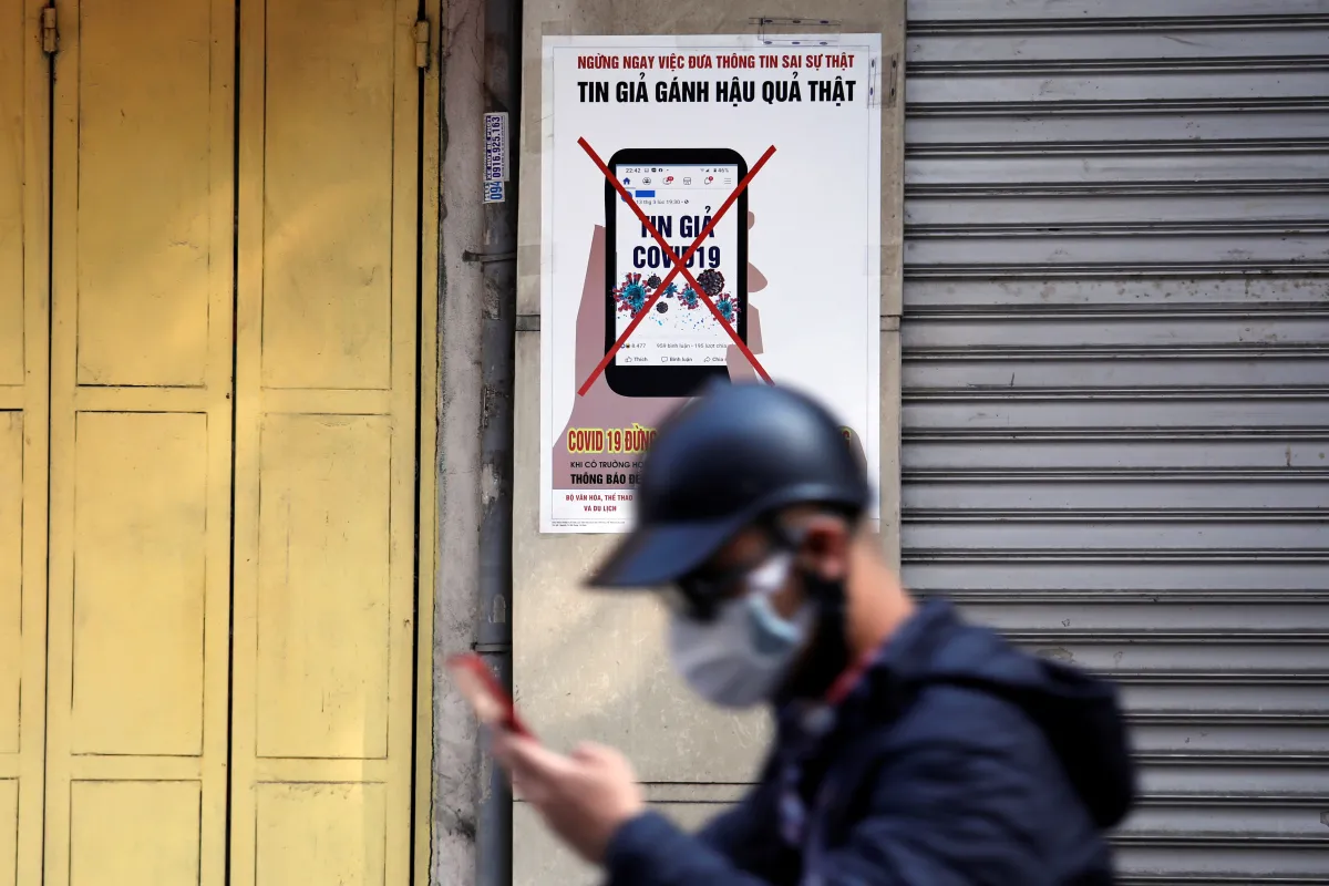 A man uses a smartphone as he walks past a poster warning against spreading 'fake news' on the coronavirus
