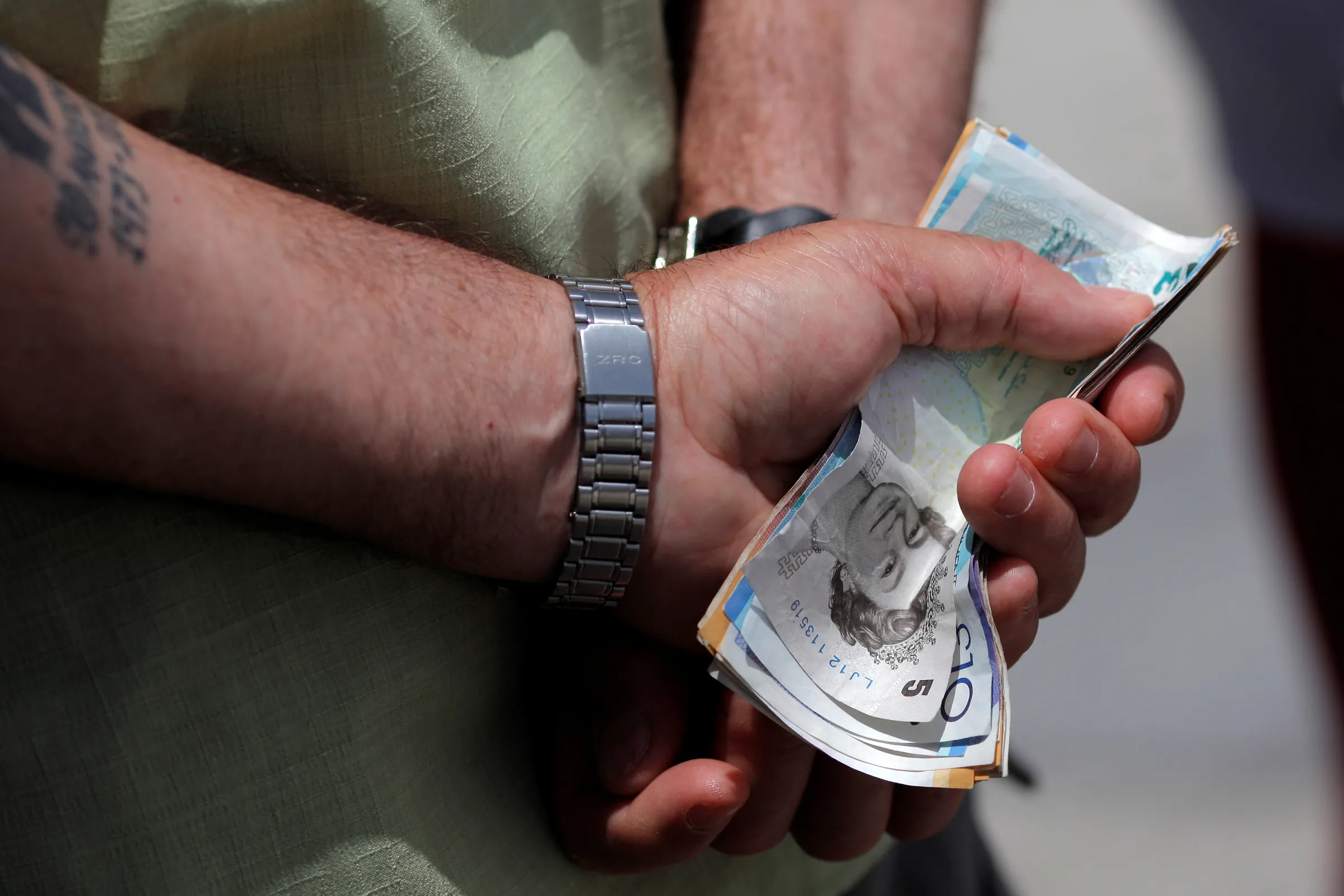 A close up of a man's hands holding various English Pound notes behind his back in the British overseas territory of Gibraltar, June 24, 2016, REUTERS/Jon Nazca