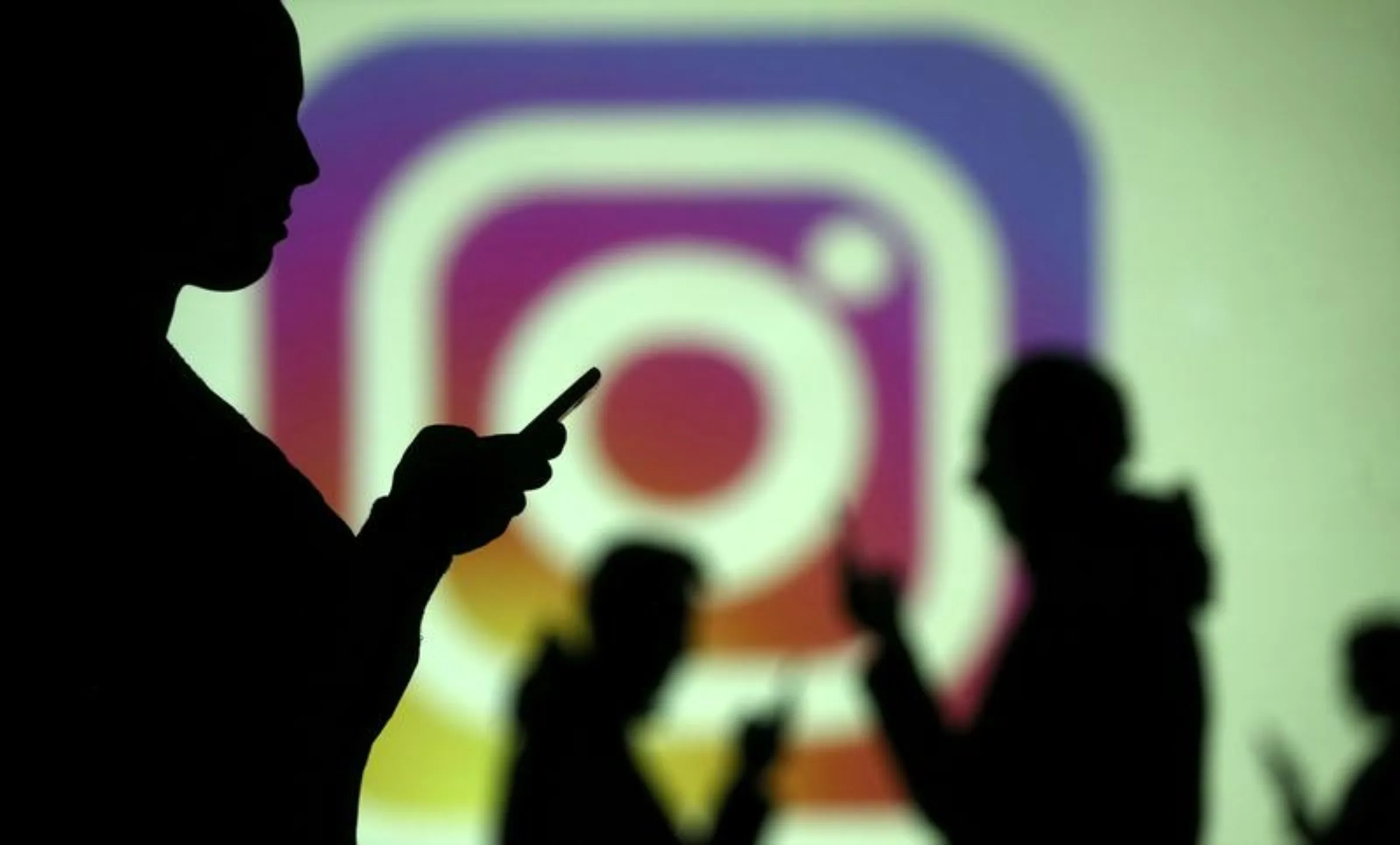 Silhouettes of mobile users are seen next to a screen projection of Instagram logo in this picture illustration taken March 28, 2018. REUTERS/Dado Ruvic/Illustration