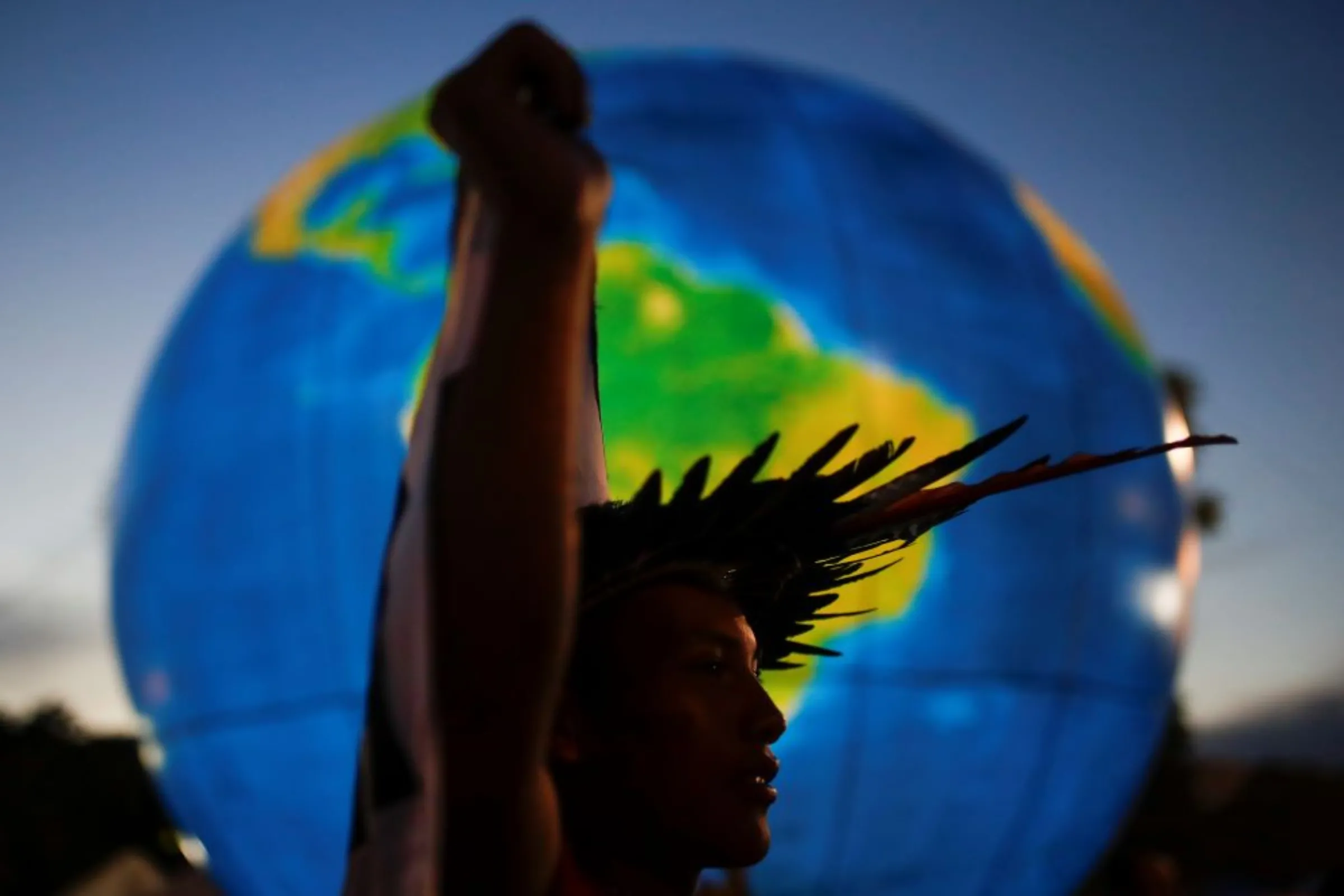 An indigenous man, holds a banner in front of a globe at the Terra Livre (Free Land) camp, a protest-camp to defend indigenous land and cultural rights, in Brasilia, Brazil April 8, 2022