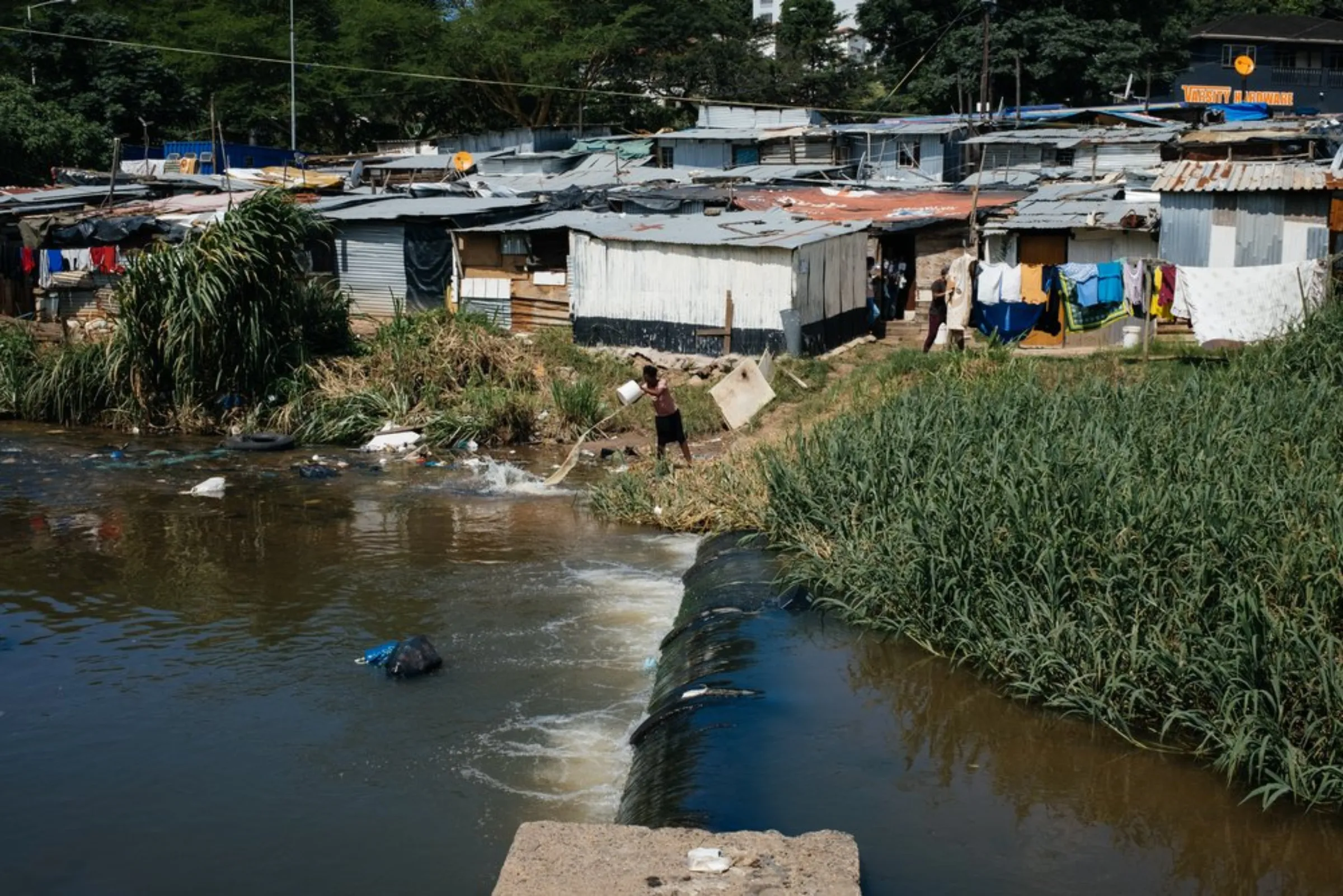 A resident of the Quarry Road informal settlement discards a bucket of water into the Palmiet River in Durban, South Africa, March 30, 2021