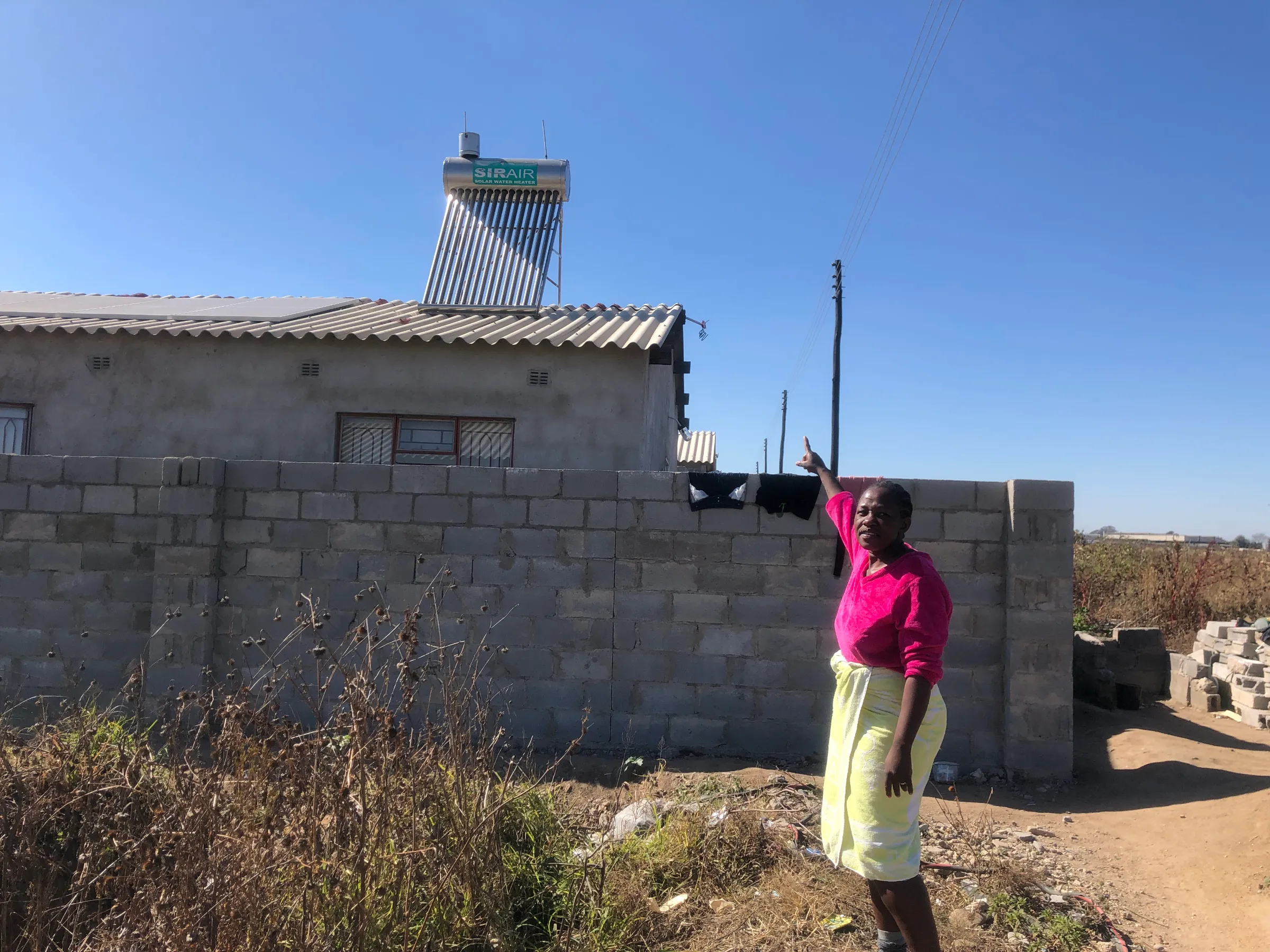 A woman points at the roof of her house which has a solar heater on top