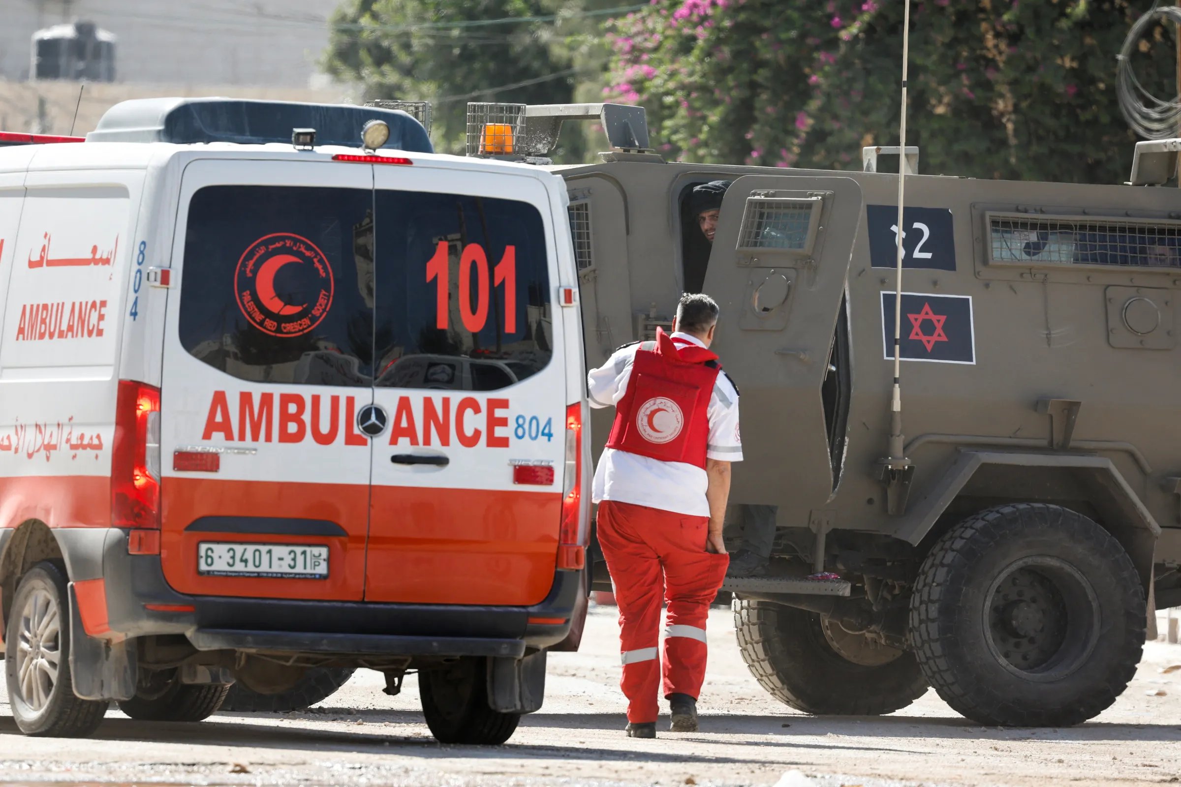 A member of the Palestine Red Crescent Society (PRCS) walks near an ambulance and Israeli military vehicle, during a raid, in Jenin, in the Israeli-occupied West Bank, August 28, 2024. REUTERS/Raneen Sawafta