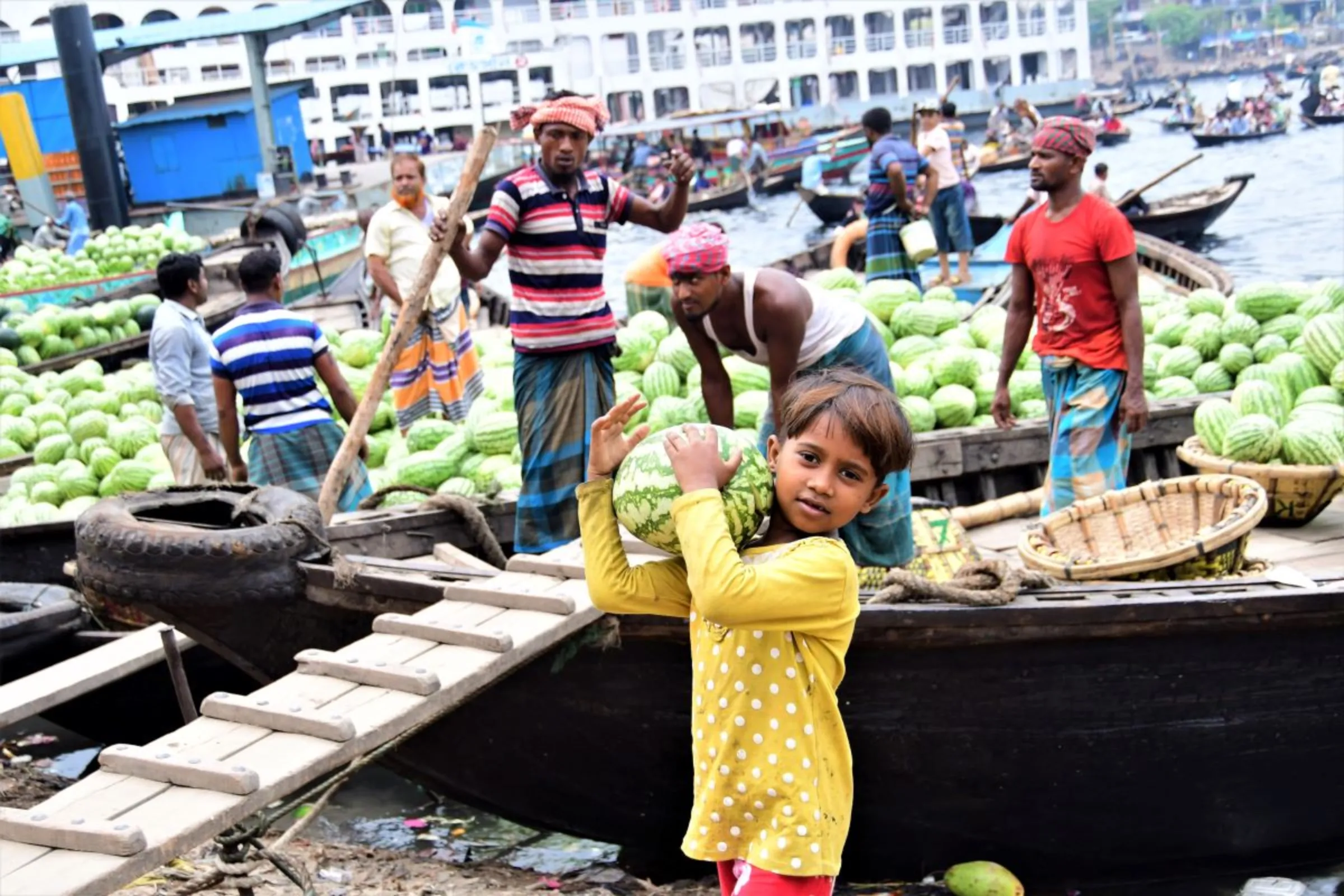 Rupa, 9, who migrated to an urban slum last year after a cyclone destroyed her rural home, unloads watermelons at Sadarghat, a wharf near Dhaka, Bangladesh, March 22, 2022. Thomson Reuters Foundation/Mosabber Hossain