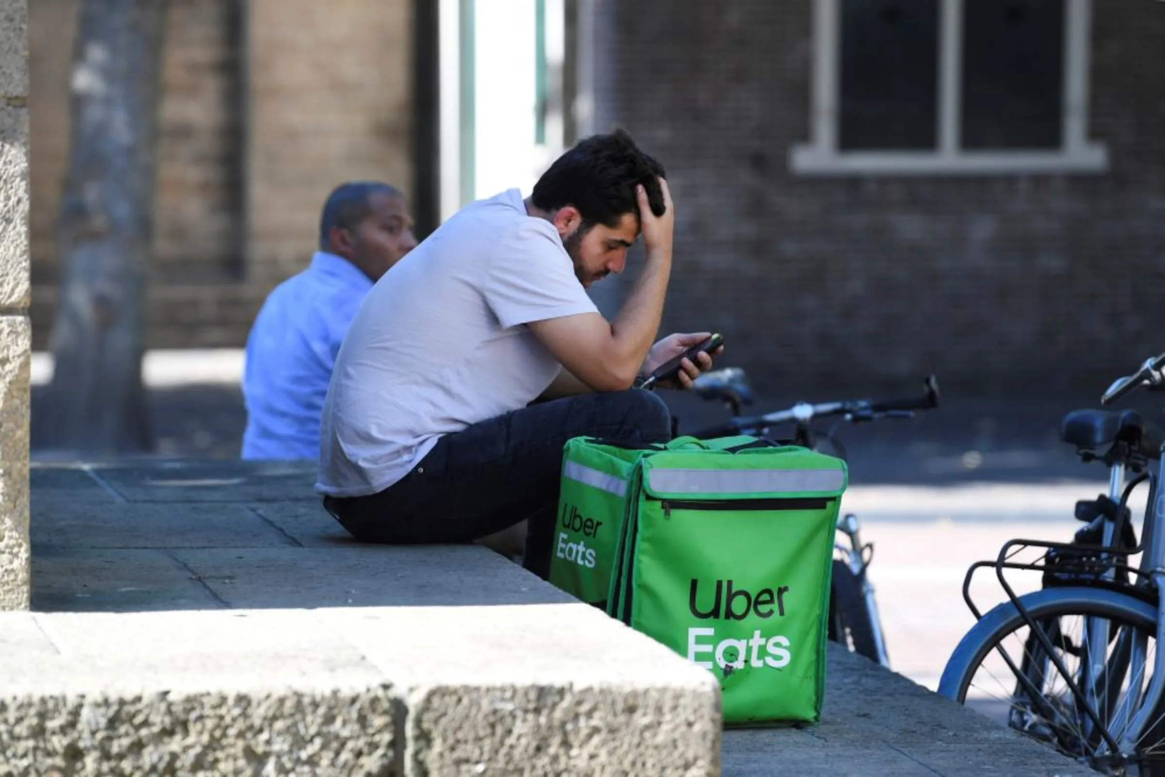 A bicycle courier from Uber Eats checks his phone in the shade during the heatwave in Utrecht , Netherlands August 10, 2022. REUTERS/Piroschka van de Wouw