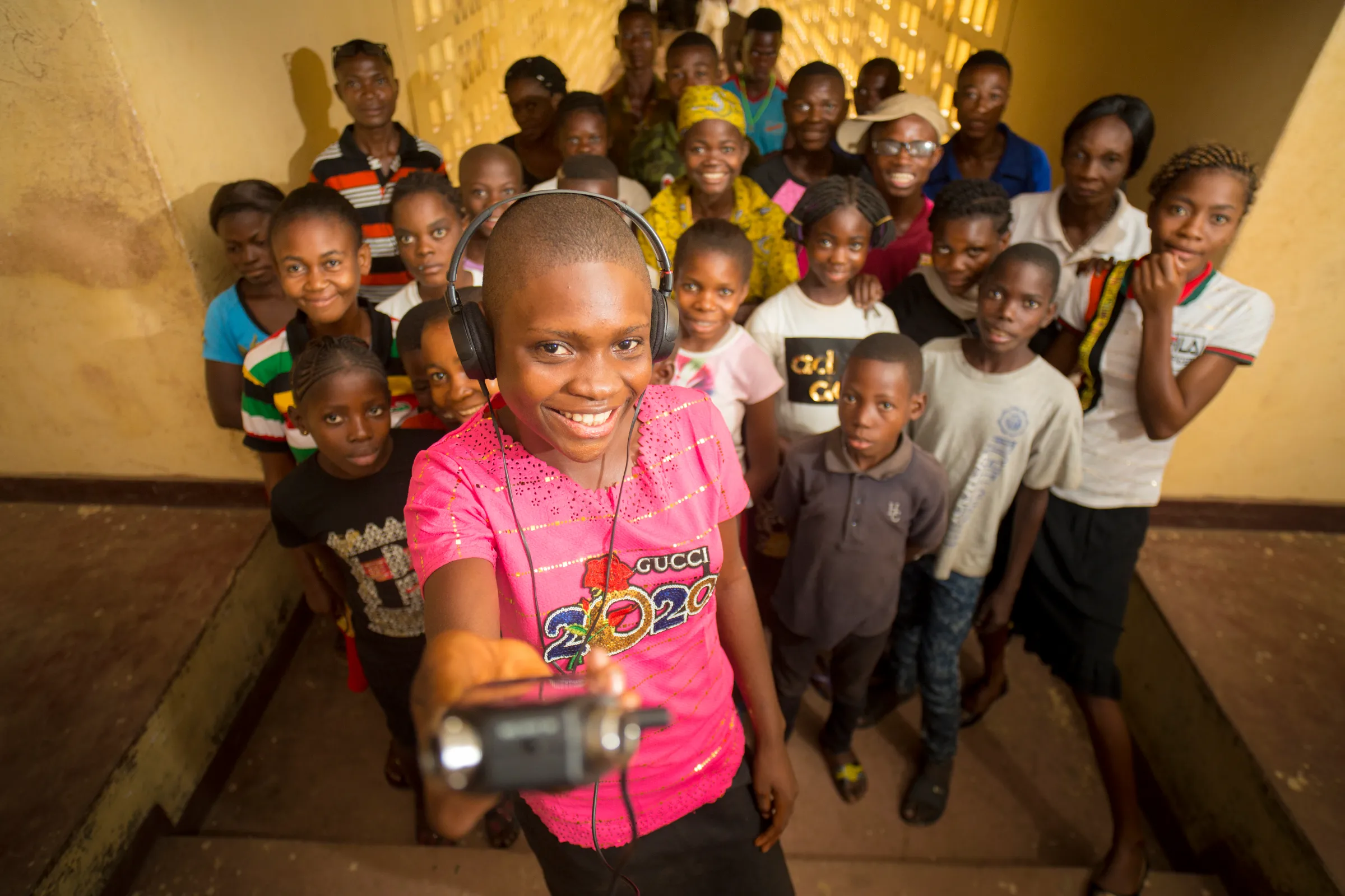 A young reporter smiles at the camera with a recorder in her hand while members of her community gather behind her in Kinshasa, The Democratic Republic of Congo, June 28, 2016. Rowan Pybus/Handout via Thomson Reuters Foundation