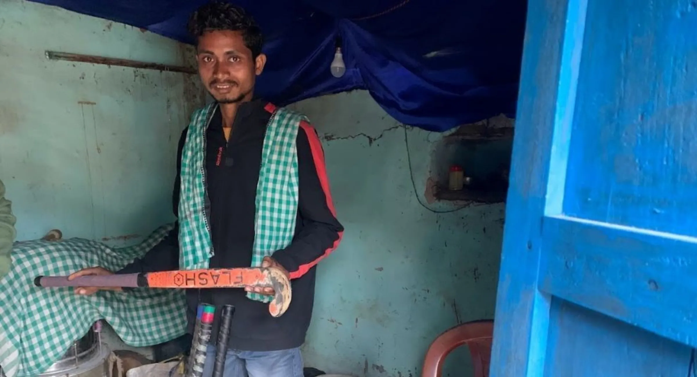 Bimal Ashok Minj poses with a hockey stick in Sumura village in Odisha state, December 10, 2022