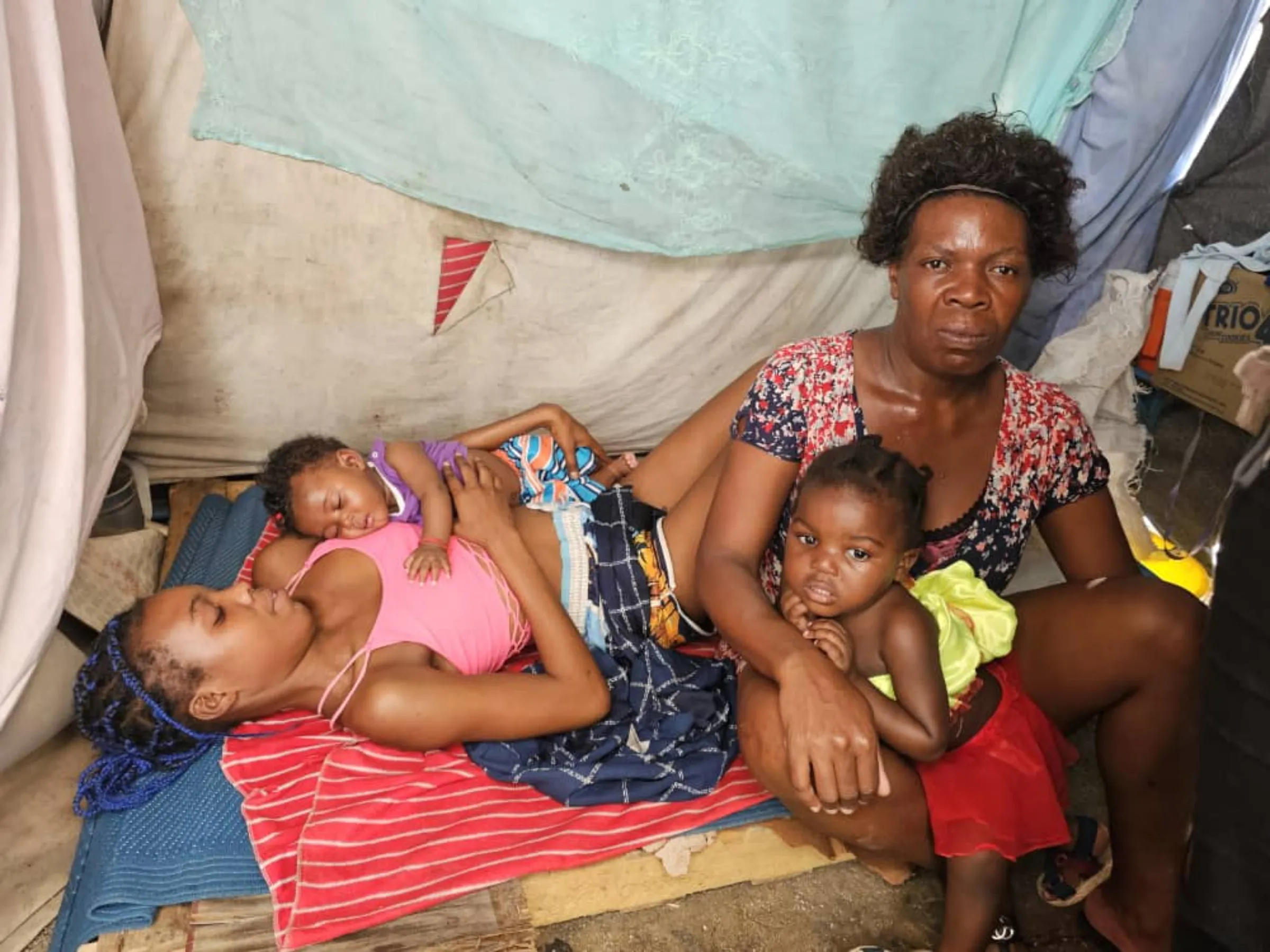Briana Casimir lying down with her daughter and beside her mother in a tent in the Darius Denis camp in Lalue, Port-au-Prince, Haiti. March 7, 2025. Thomson Reuters Foundation/Joseph Guyler Delva