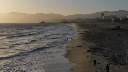 GIF of a landscape of the sea during sunset with mountains in the background and people walking along the beach