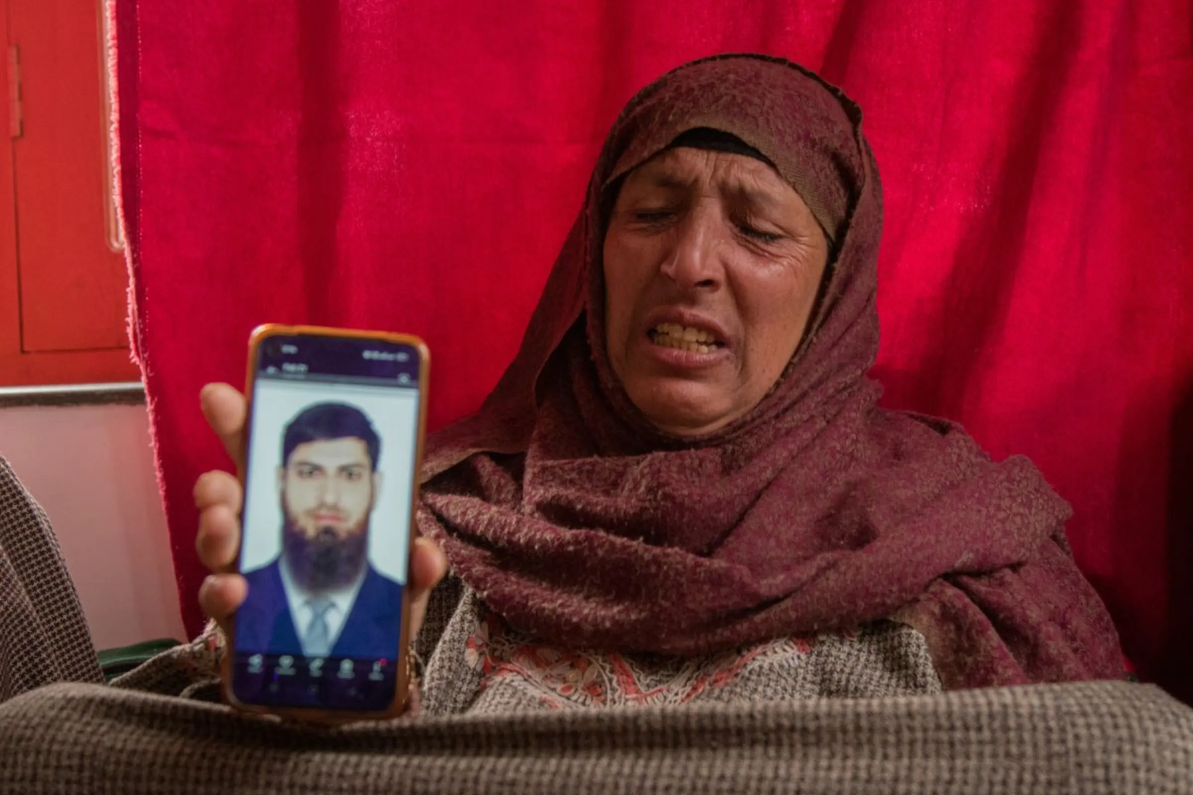 The mother of Azad Yousuf Kumar, who got duped into fighting in the Russia-Ukraine war, cries while showing a photo of her son on her mobile phone at their home in Poshwan, Kashmir, Febraury 28, 2024. Thomson Reuters Foundation/Umer Farooq