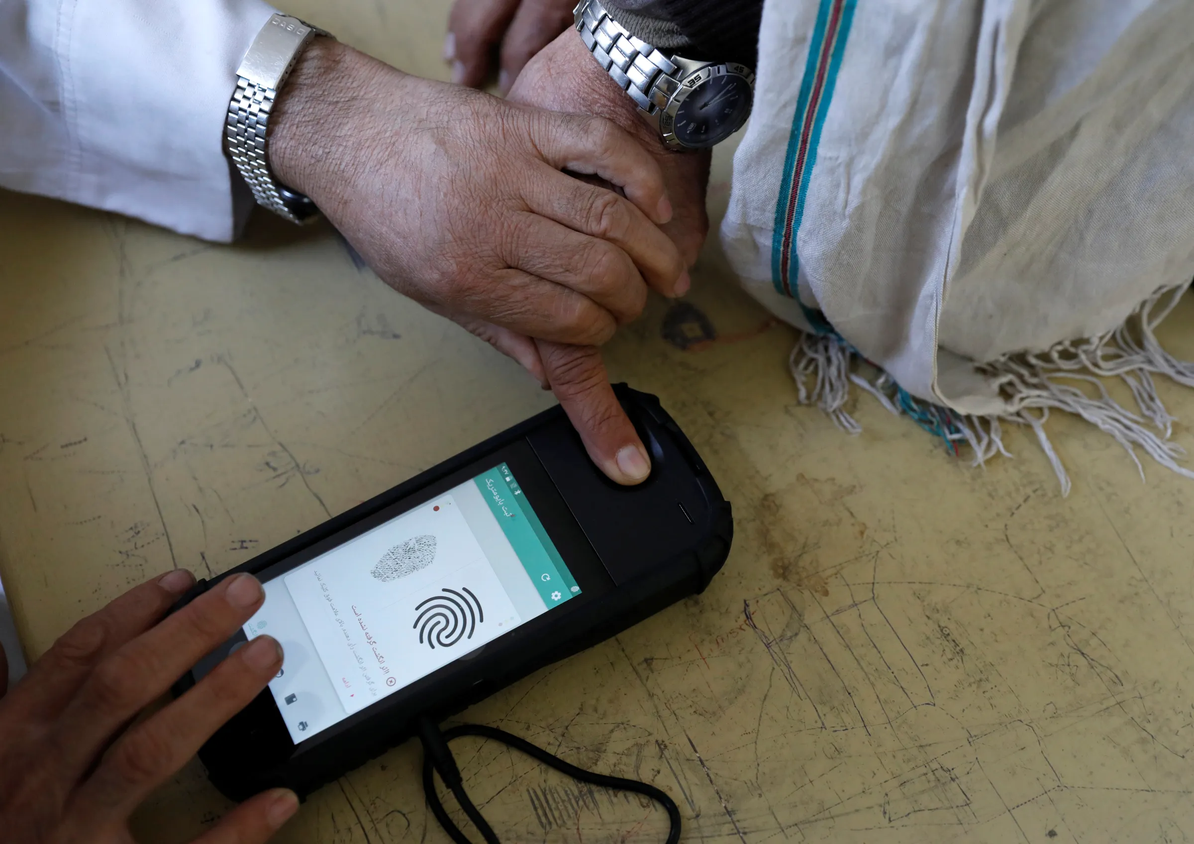 An election official scans a voter's finger with a biometric device at a polling station