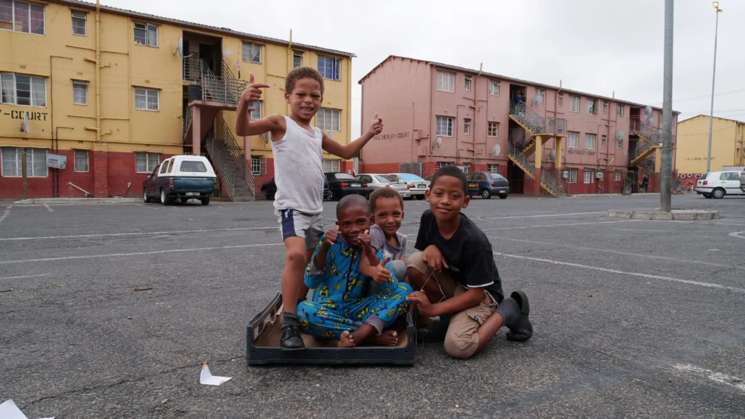 Four young children pose for a photo as they sit on a plastic crate in the parking lot of apartment blocks in the Scottsdene neighbourhood in Cape Town, South Africa, March 9, 2023. Thomson Reuters Foundation/Kim Harrisberg