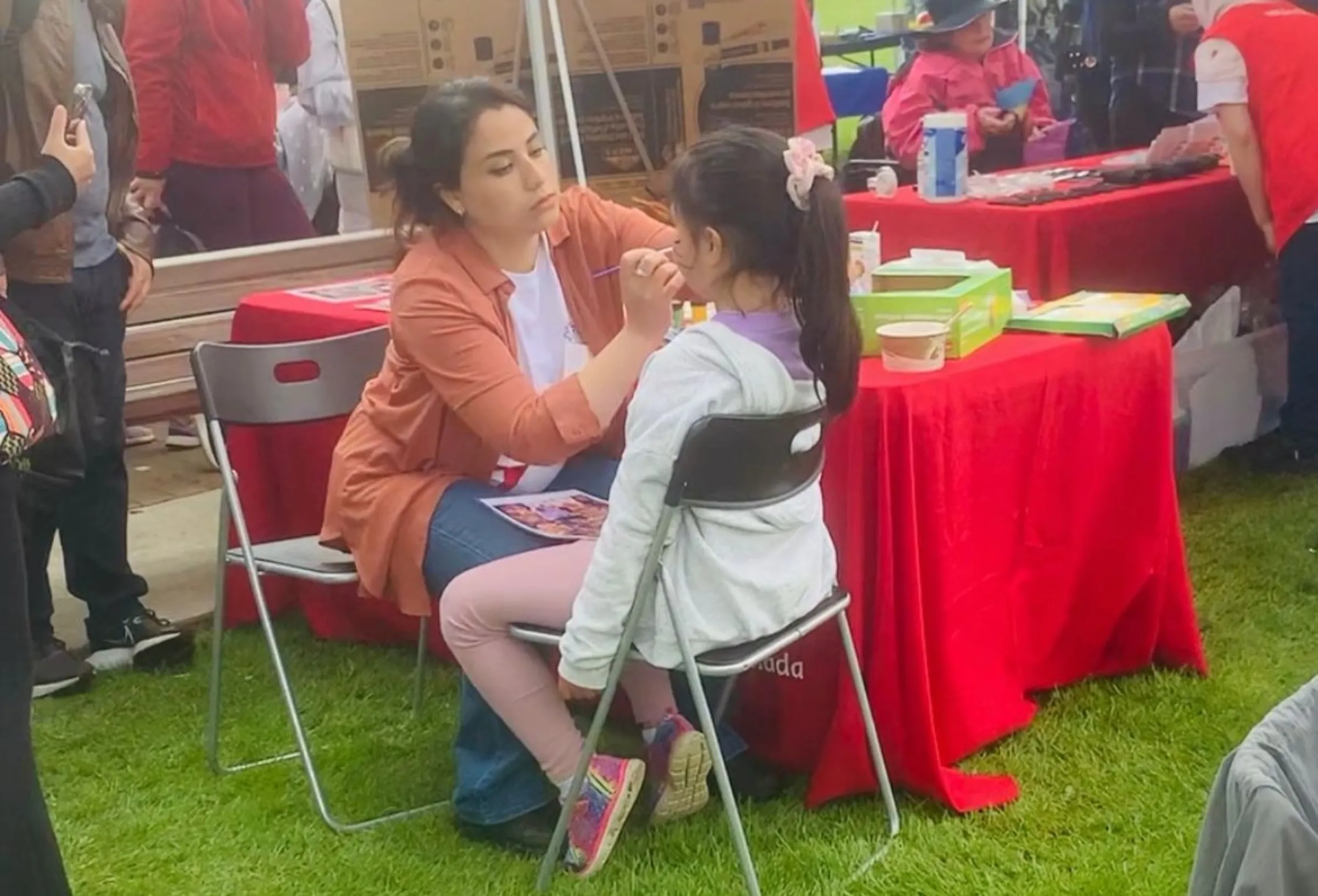 A woman paints the face of a girl sat at a table at a fair in Vancouver