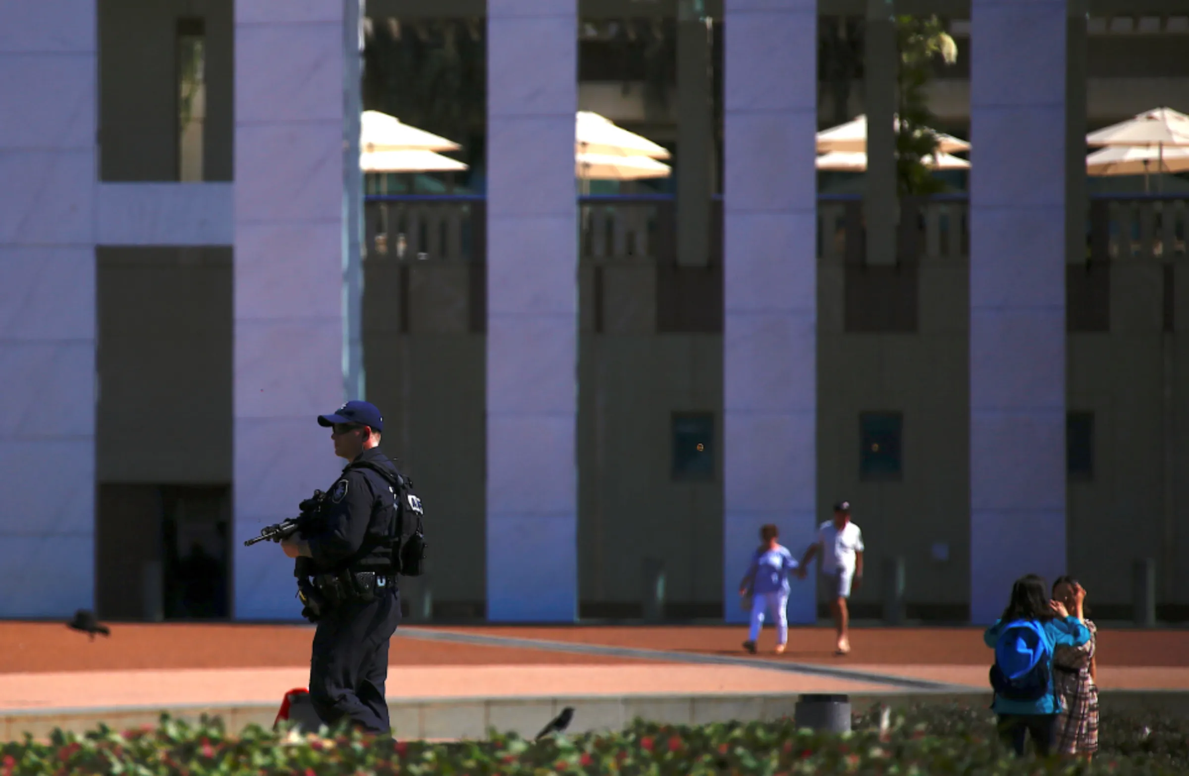 Tourists take photographs and walk near an Australian Federal policeman carrying a gun as he patrols the forecourt of Australia's Parliament House in Canberra, Australia, October 16, 2017