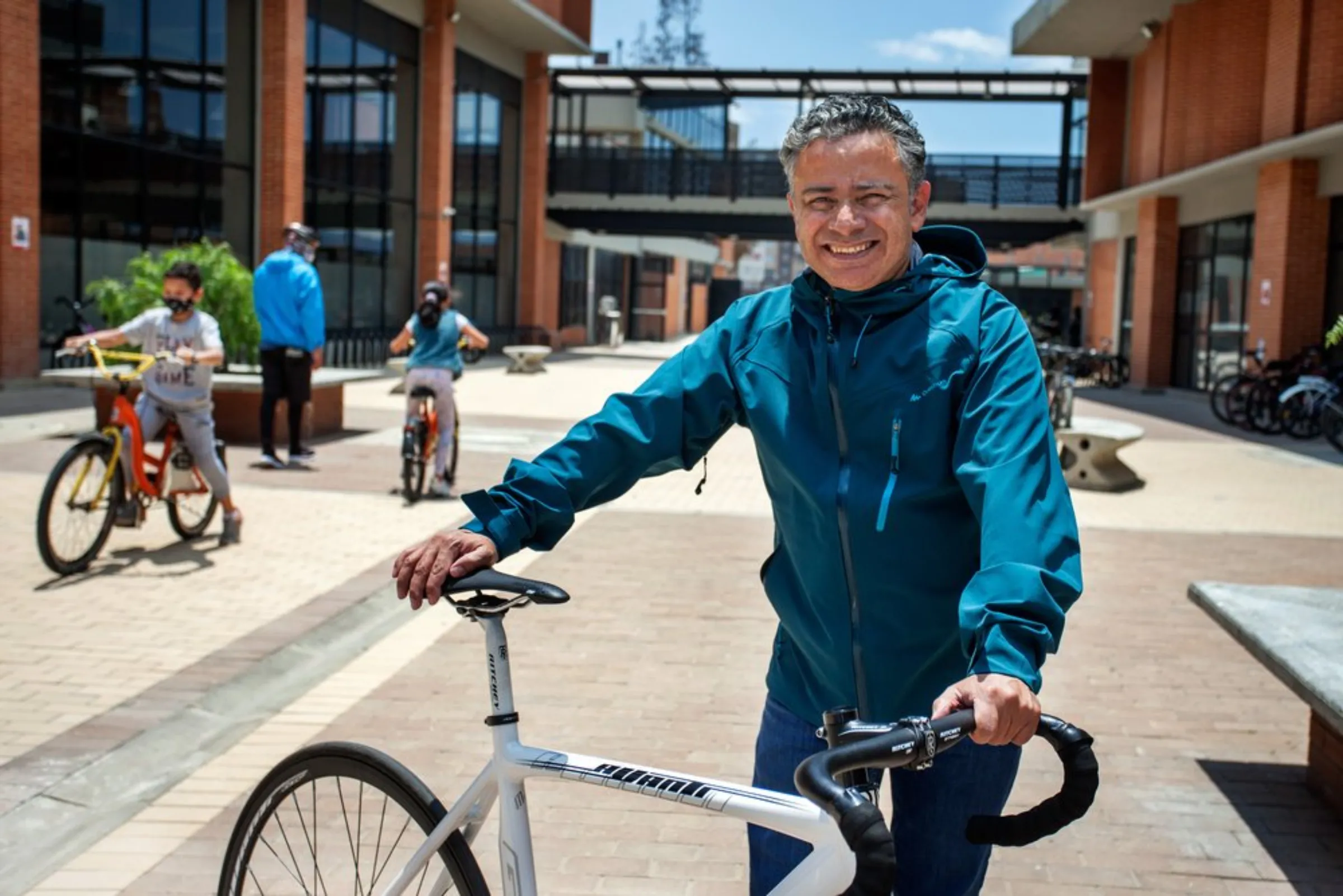 Jose Willington, headteacher at “The Bike College”, a new public school in the poor neighbourhood of Bosa, stands with his cycle as students practice riding behind him at the school in south Bogota, Colombia, April 22, 2021