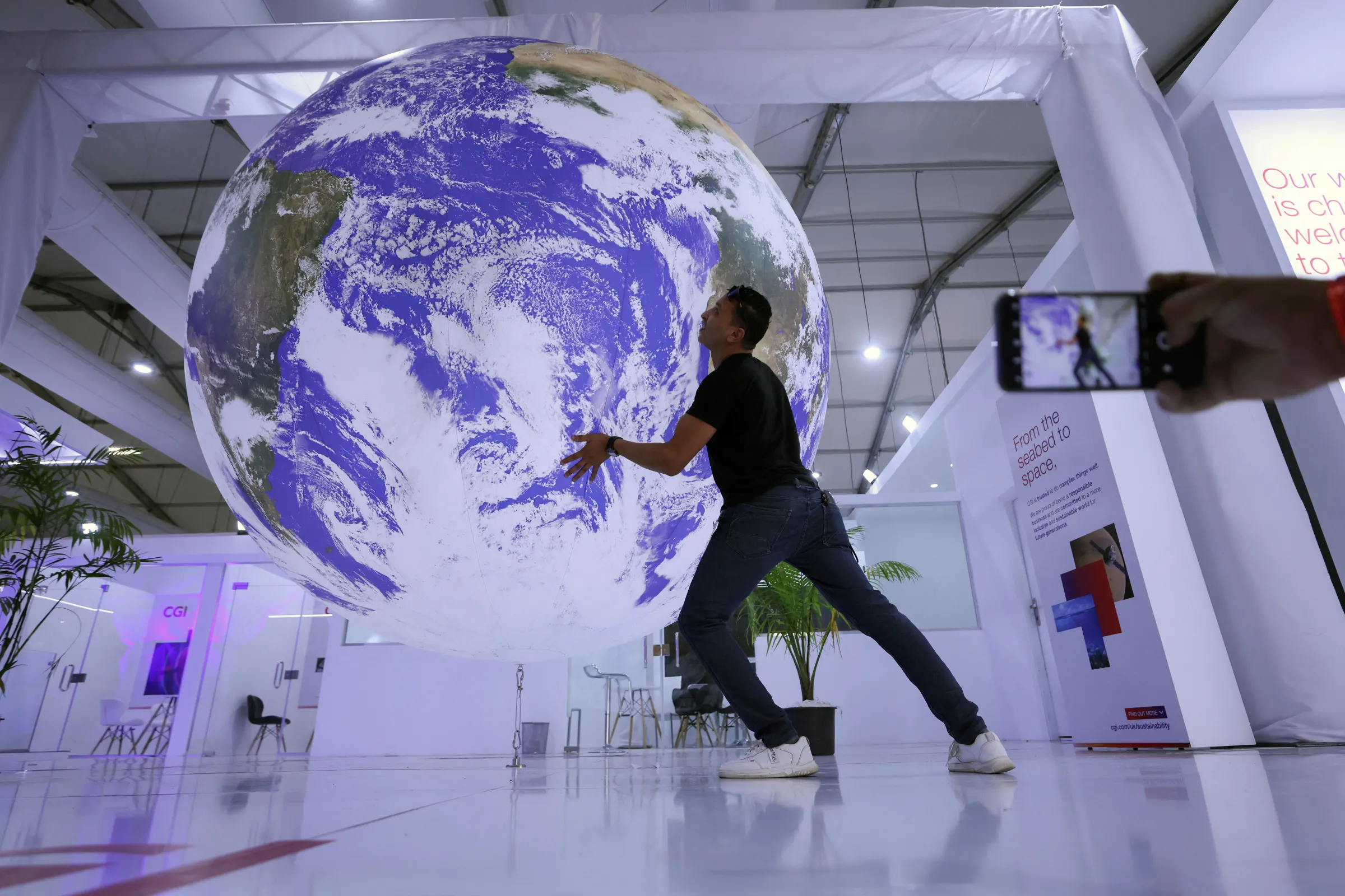 An attendee poses for a picture near a model earth during the COP27 climate summit in Sharm el-Sheikh, Egypt November 19, 2022. REUTERS/Mohamed Abd El Ghany