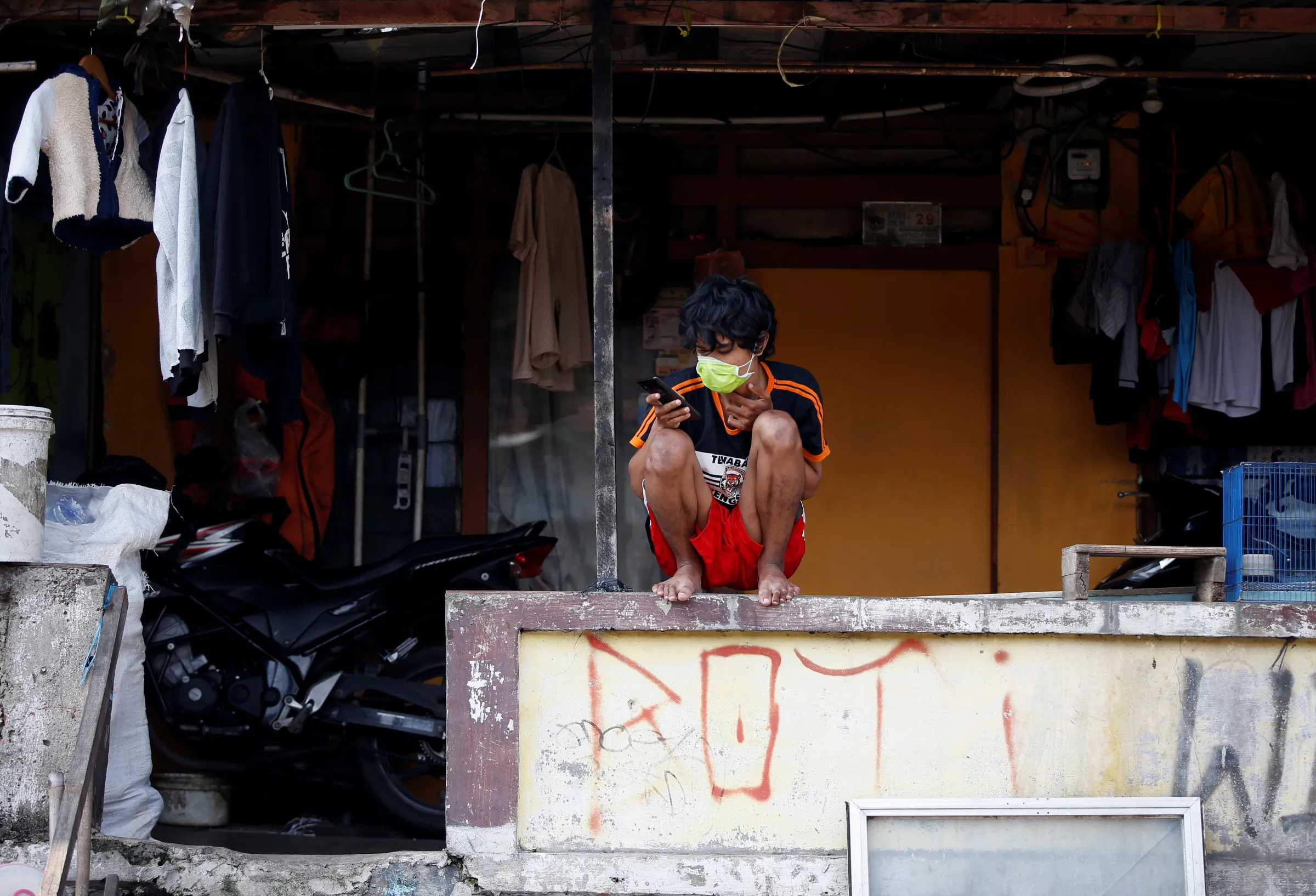 A youth wearing a protective face mask uses a phone as he sits outside his house in Jakarta, Indonesia, April 12, 2020
