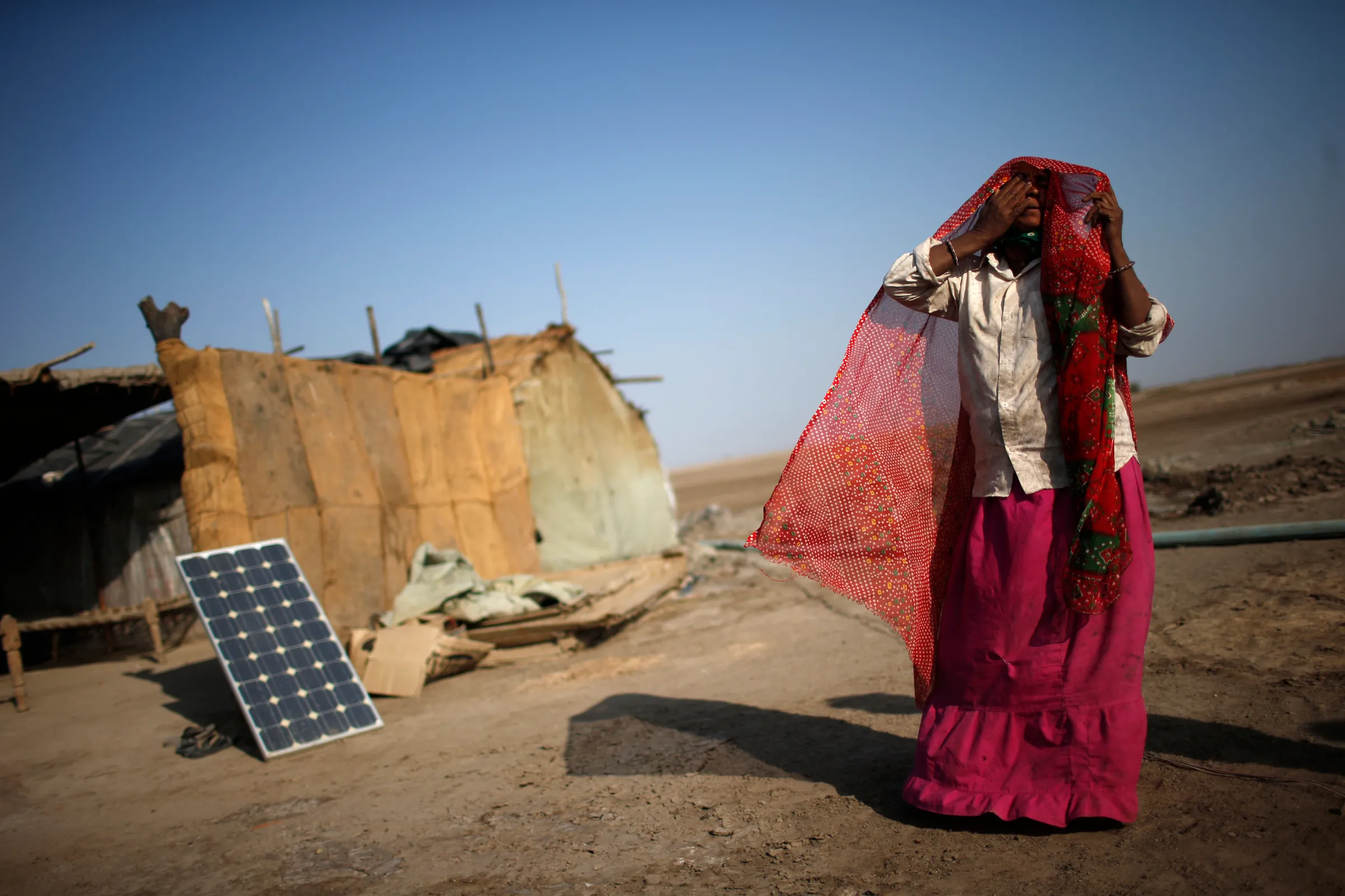 A labourer, who works in a salt pan, covers her face beside a solar panel outside a shelter in Little Rann of Kutch in the western Indian state of Gujarat March 2, 2014