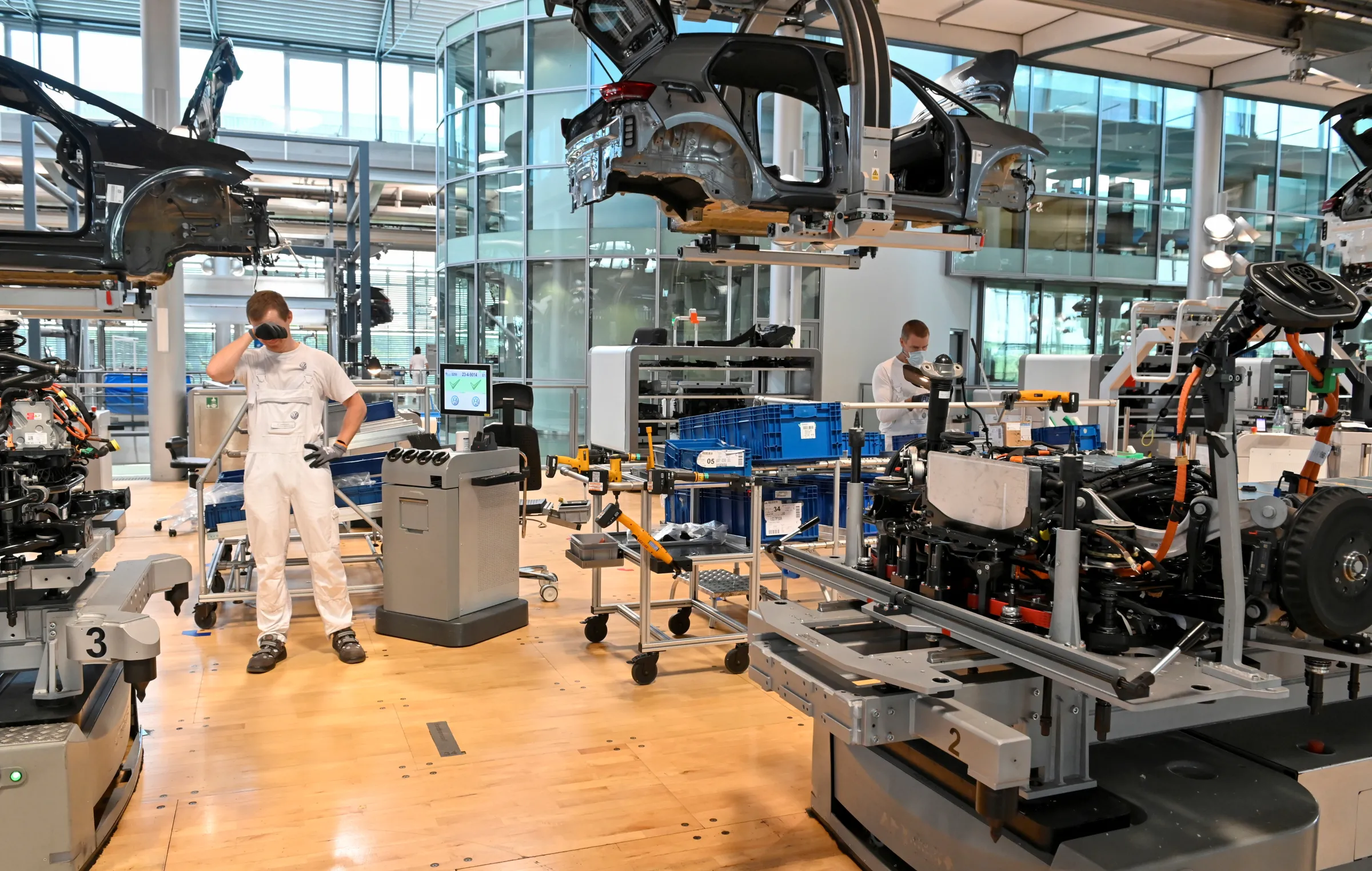 Car frames are pictured suspended in the air above machinery on a factory floor