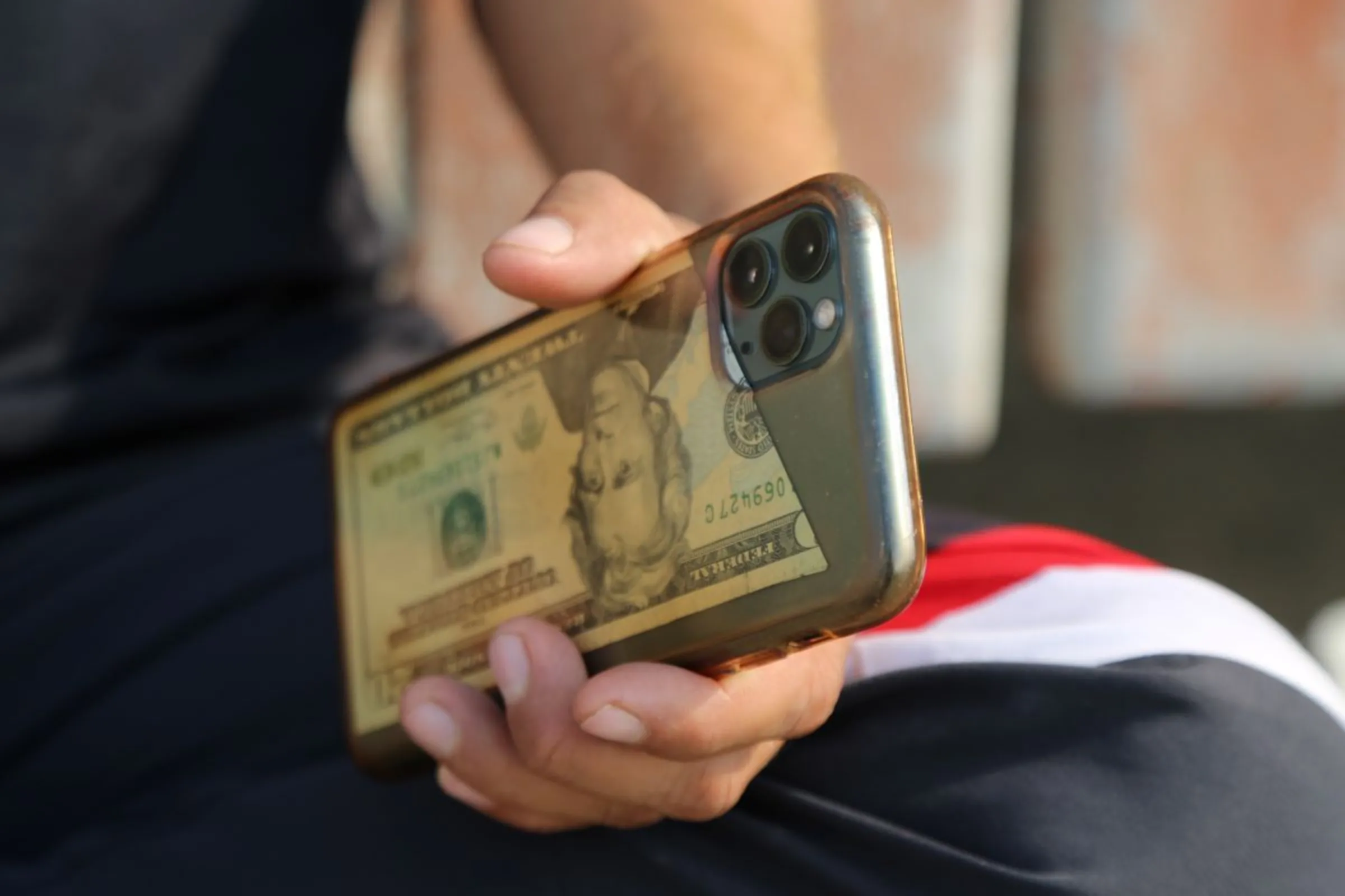 A man holds a mobile phone with a $20 bill inside its cover in Dhatrath, India, December 4, 2023. Thomson Reuters Foundation/Annie Banerji