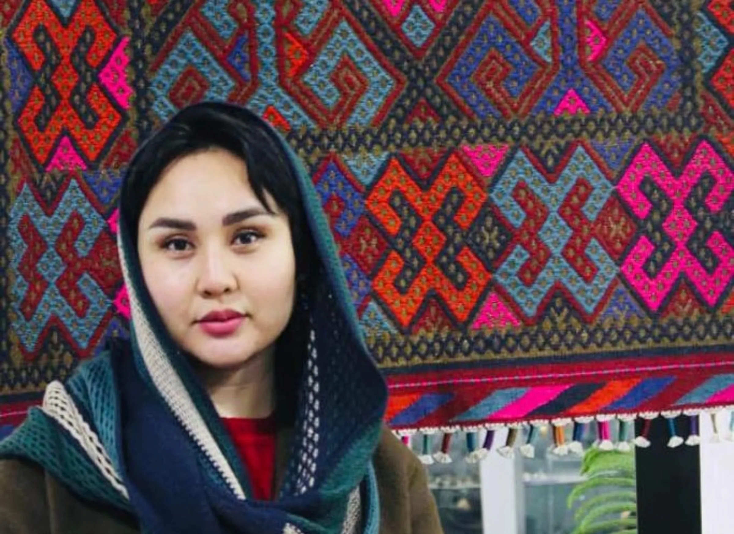 A woman stands in front of a coloured tapestry