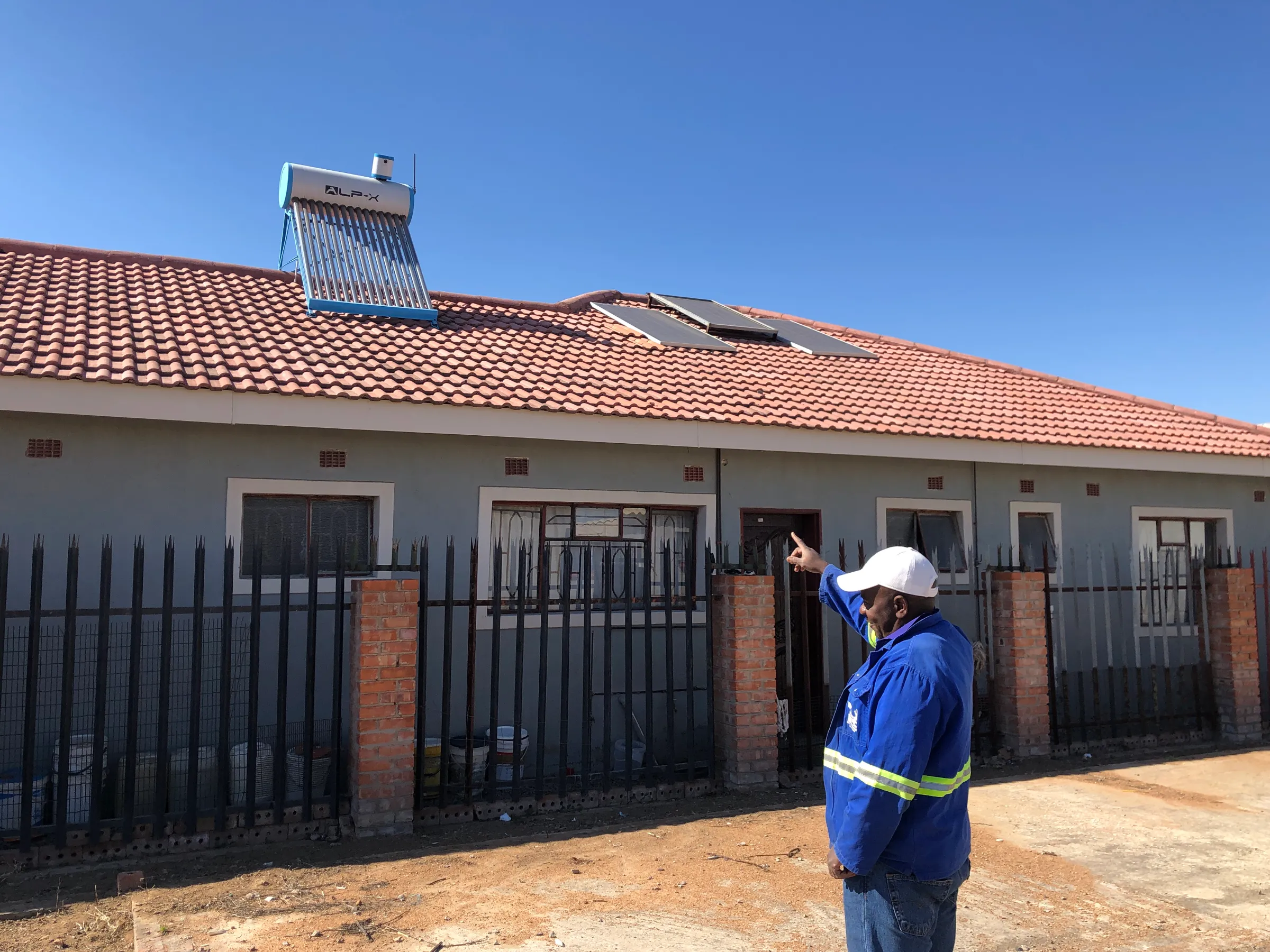 A man points at a building which has a solar heater and panels on the roof