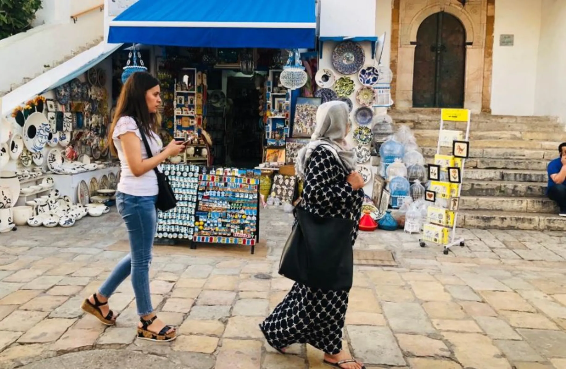 Two Tunisian women walk past a souvenir shop in Sidi Bou Said north of Tunis on June 17, 2019. Thomson Reuters Foundation/Menna A Farouk