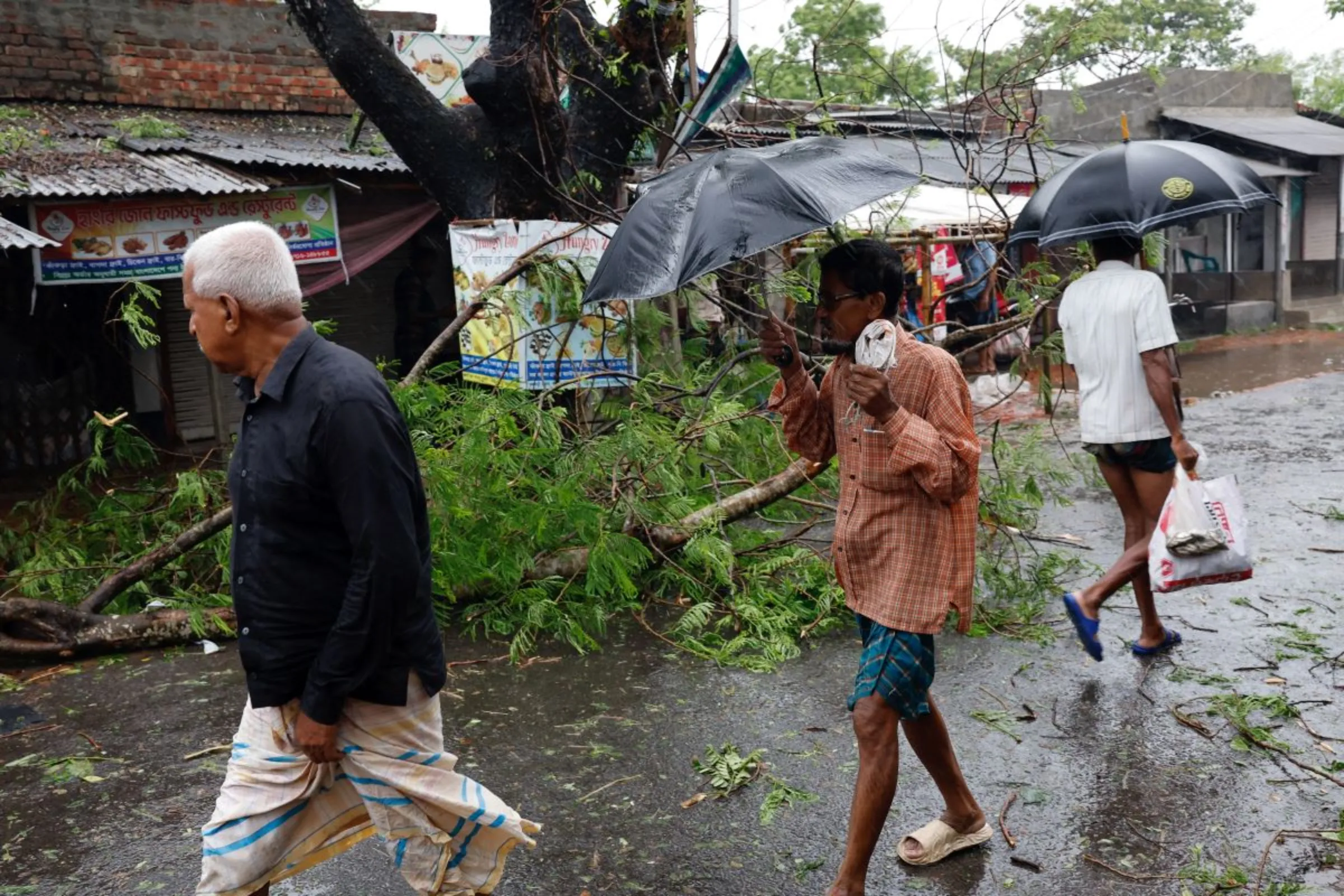 People walk past a fallen tree branch as Cyclone Remal hits Bangladesh, May 27, 2024. REUTERS/Mohammad Ponir Hossain