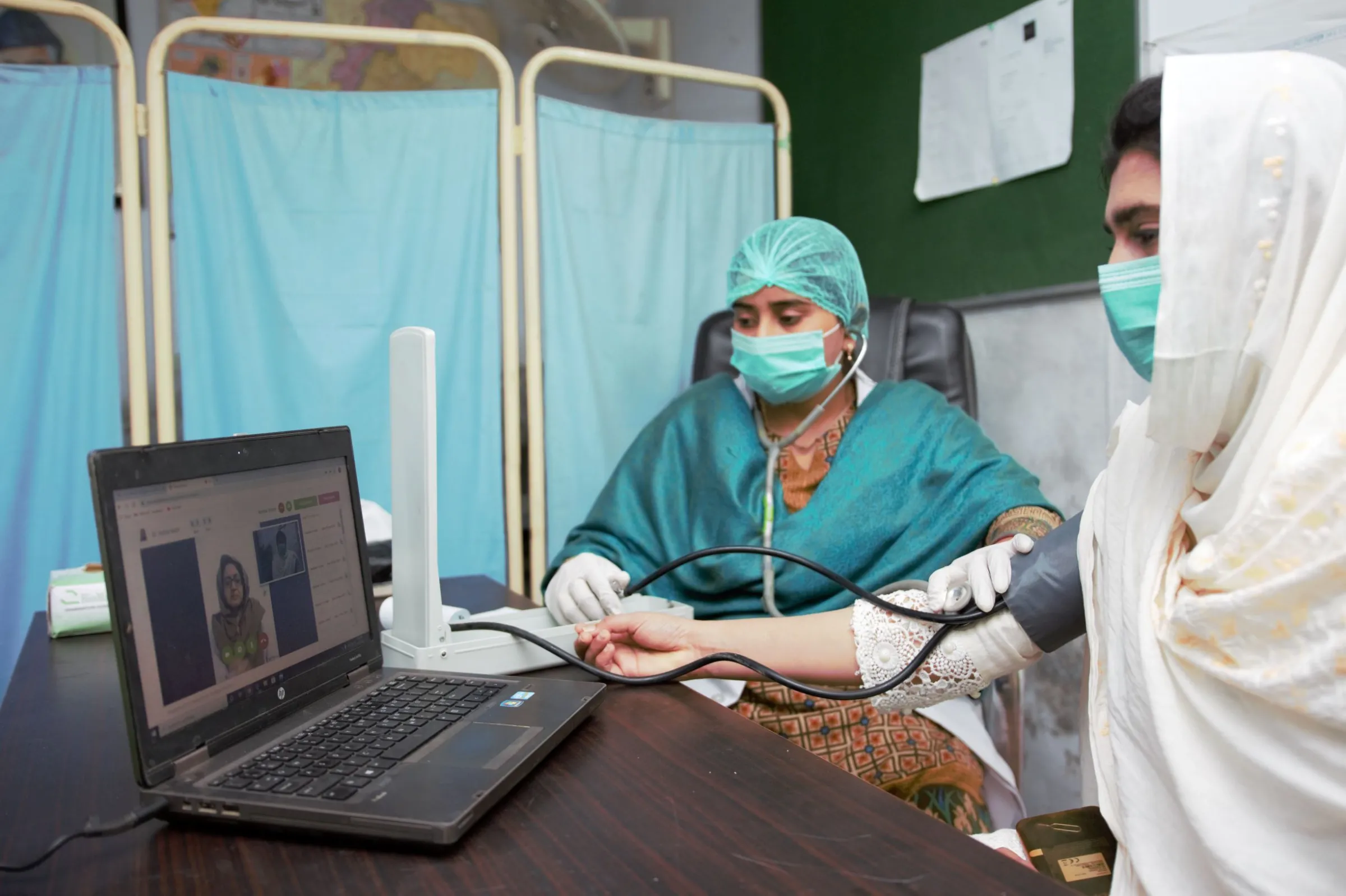 A nurse sits with a pregnant woman talking to a doctor over video call