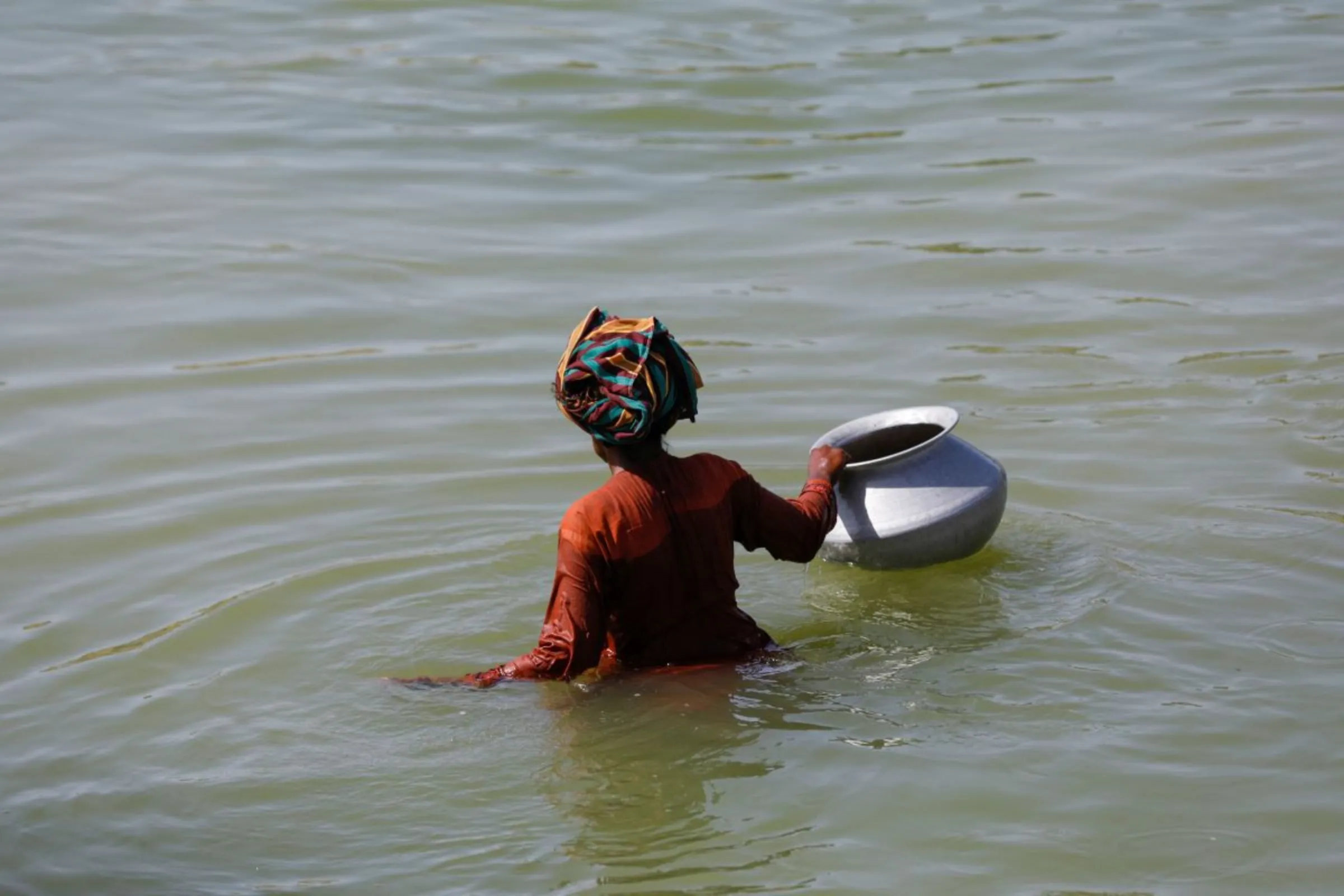 A displaced woman wades through flood water with a water pot, following rains and floods during the monsoon season in Sehwan, Pakistan, September 16, 2022