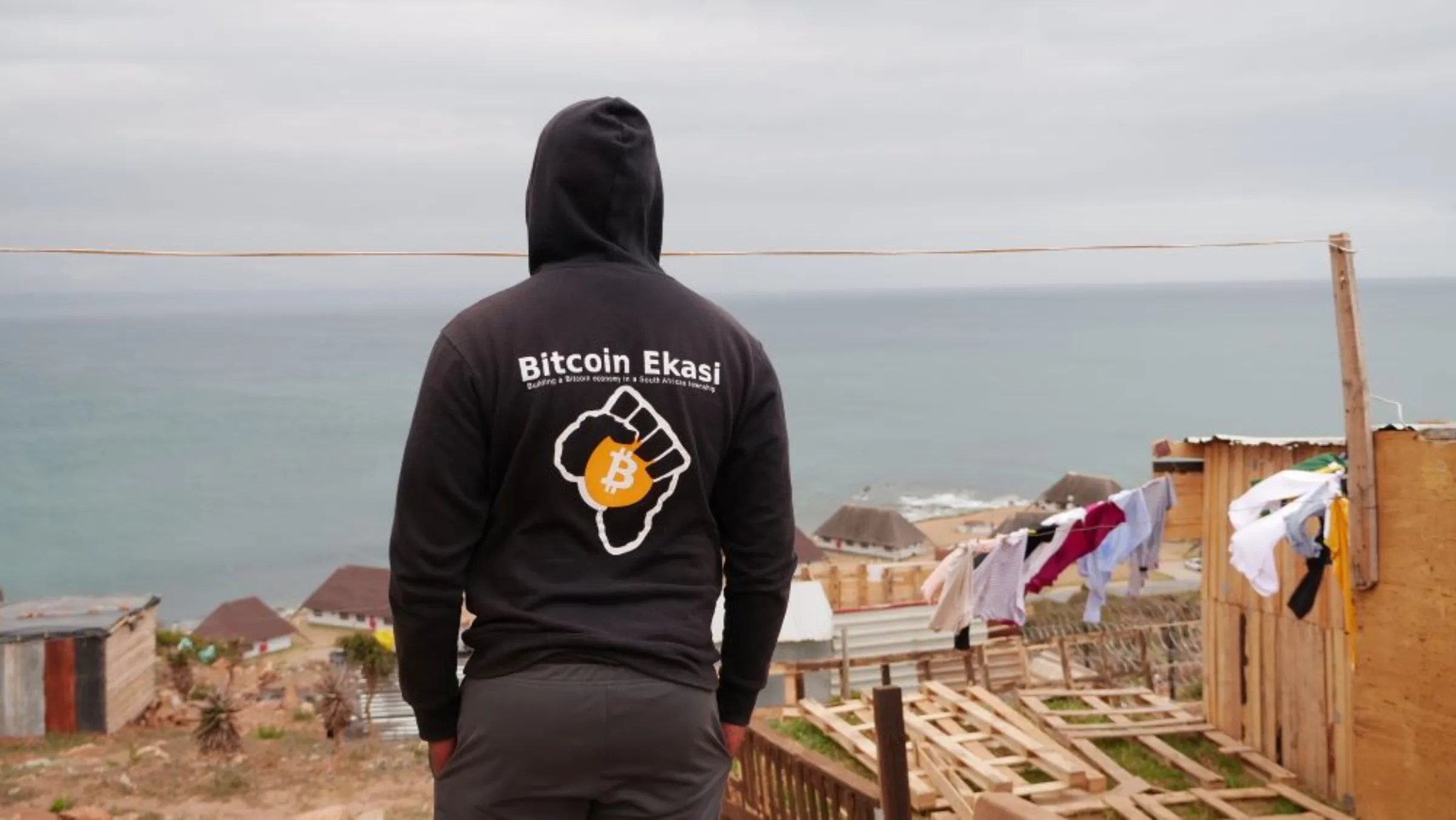 Luthando Ndabambi looks out over JCC township and the Atlantic ocean wearing his bitcoin hoodie in Mossel Bay, South Africa, November 24, 2022